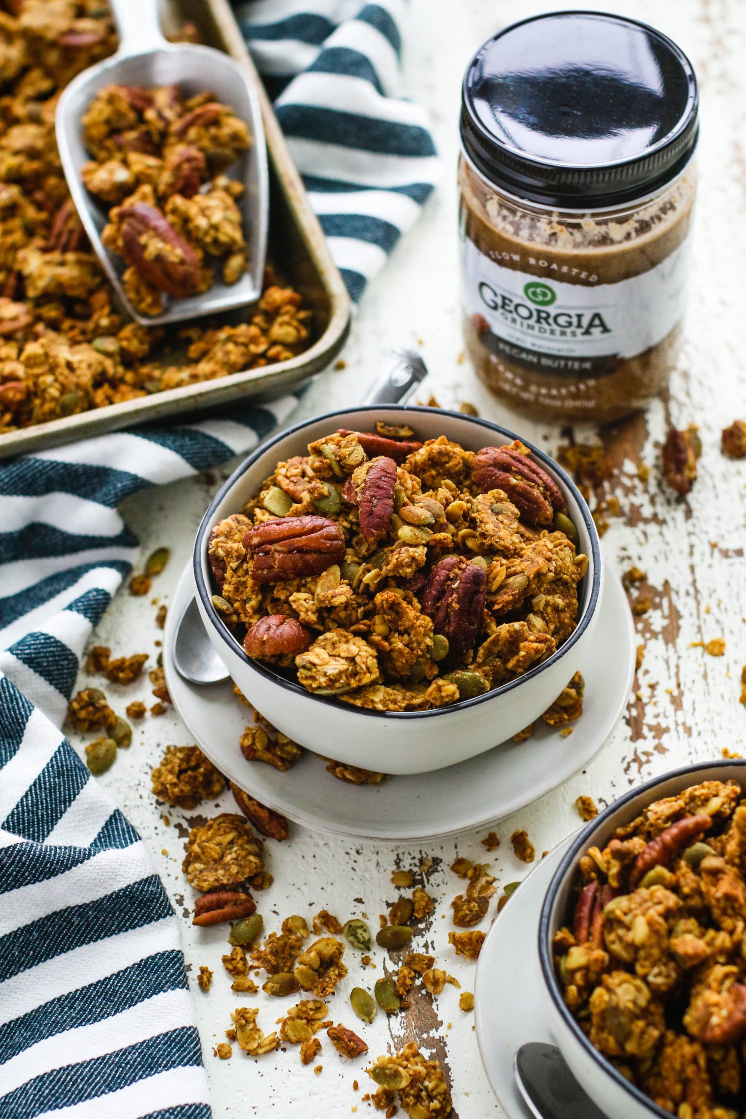 Pumpkin Spice Pecan Granola served in bowls with baking sheet in background by Flora & Vino