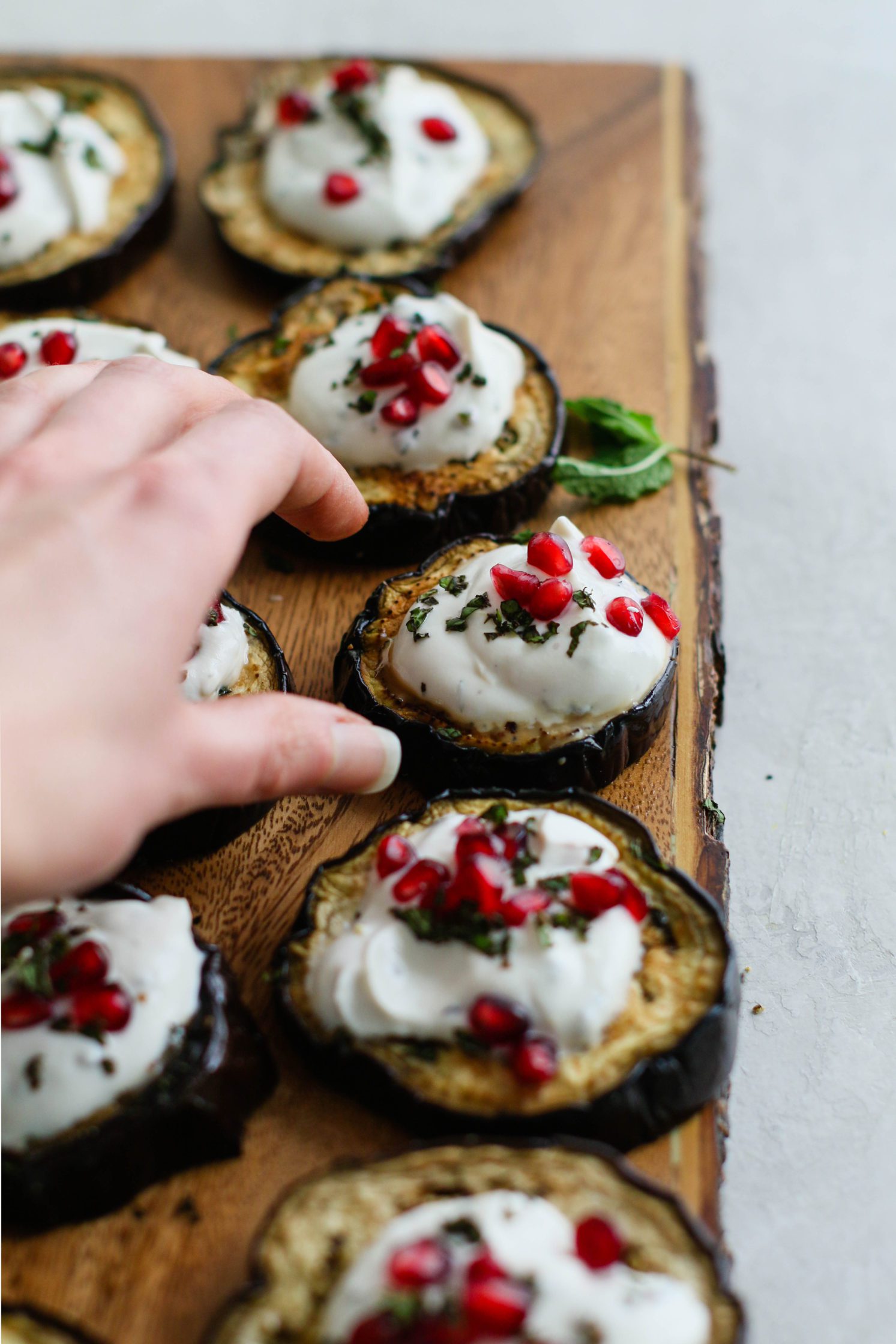 hand reaching for Eggplant Round topped with Herbed Yogurt Sauce & Pomegranate by Flora & Vino
