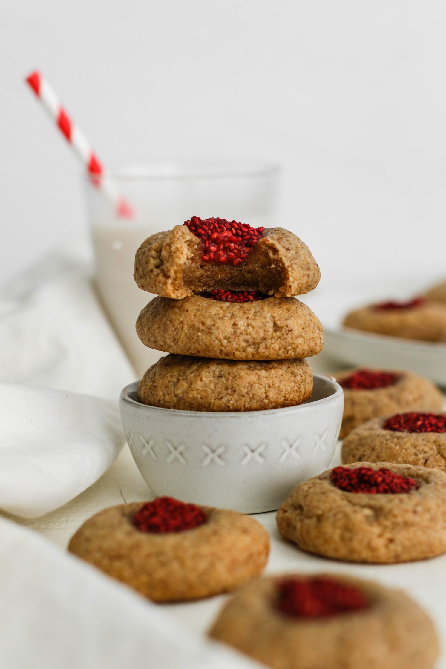 Raspberry-Beet Almond Flour Thumbprint Cookies stacked with milk and straw behind them by Flora & Vino