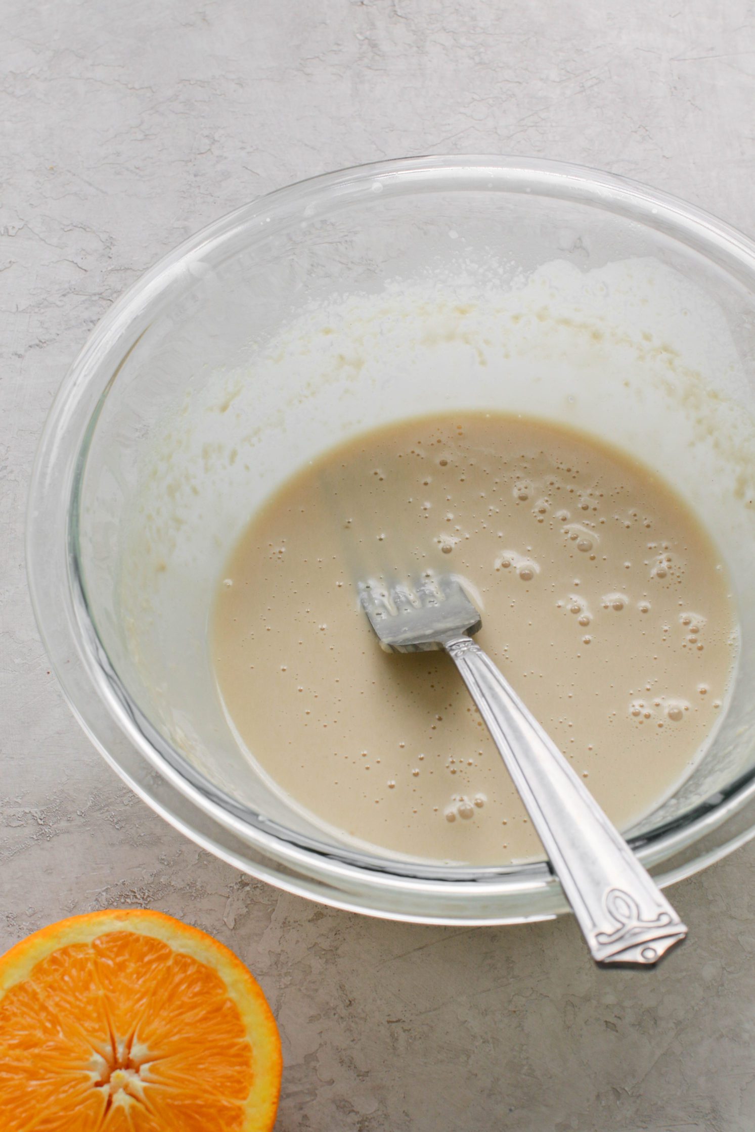 Easy Orange Tahini dressing mixed up in a glass bowl with a fork by Flora & Vino
