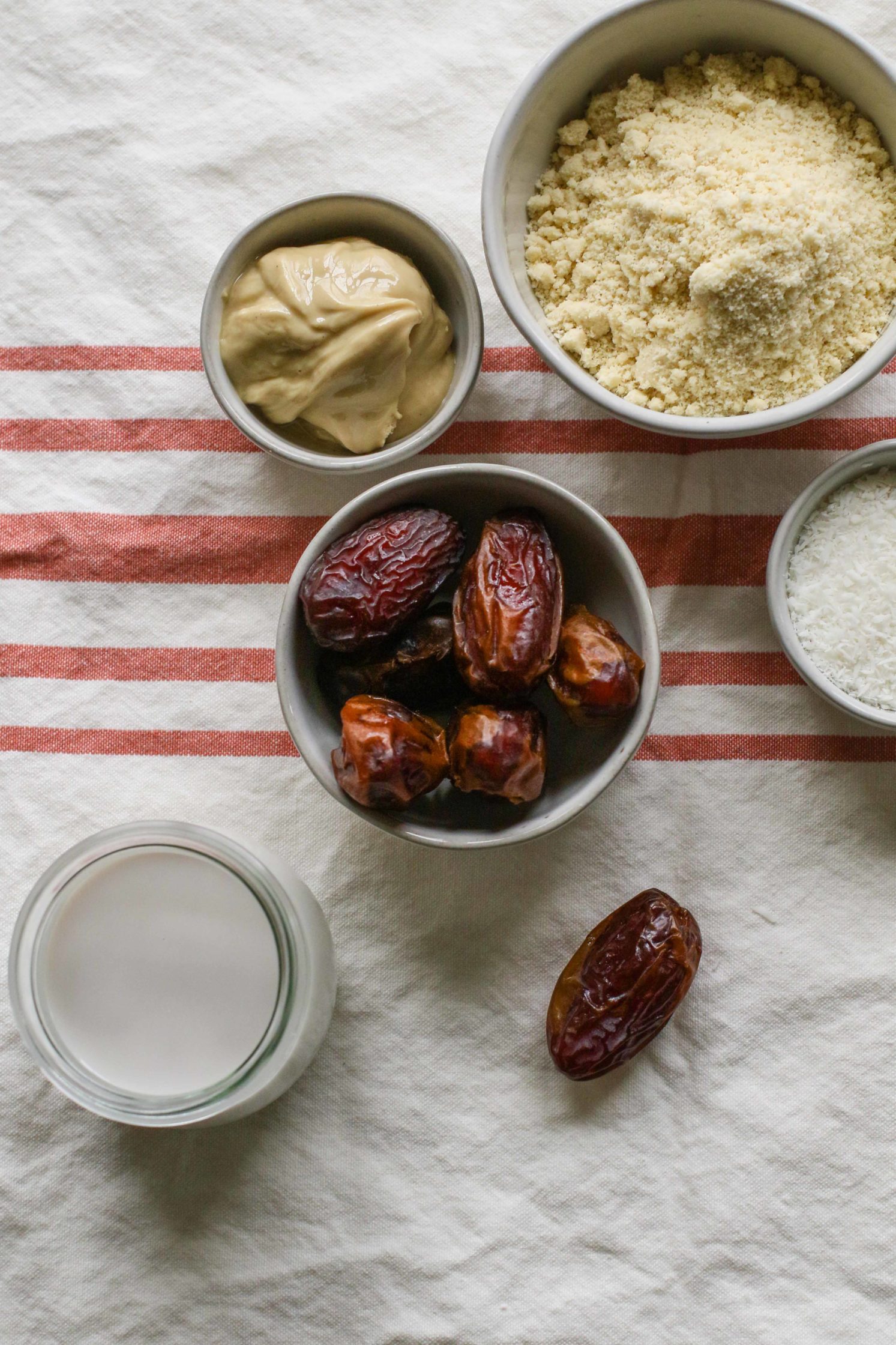Medjool dates, almond flour, cashew butter, shredded coconut, and almond milk on towel by Flora & Vino