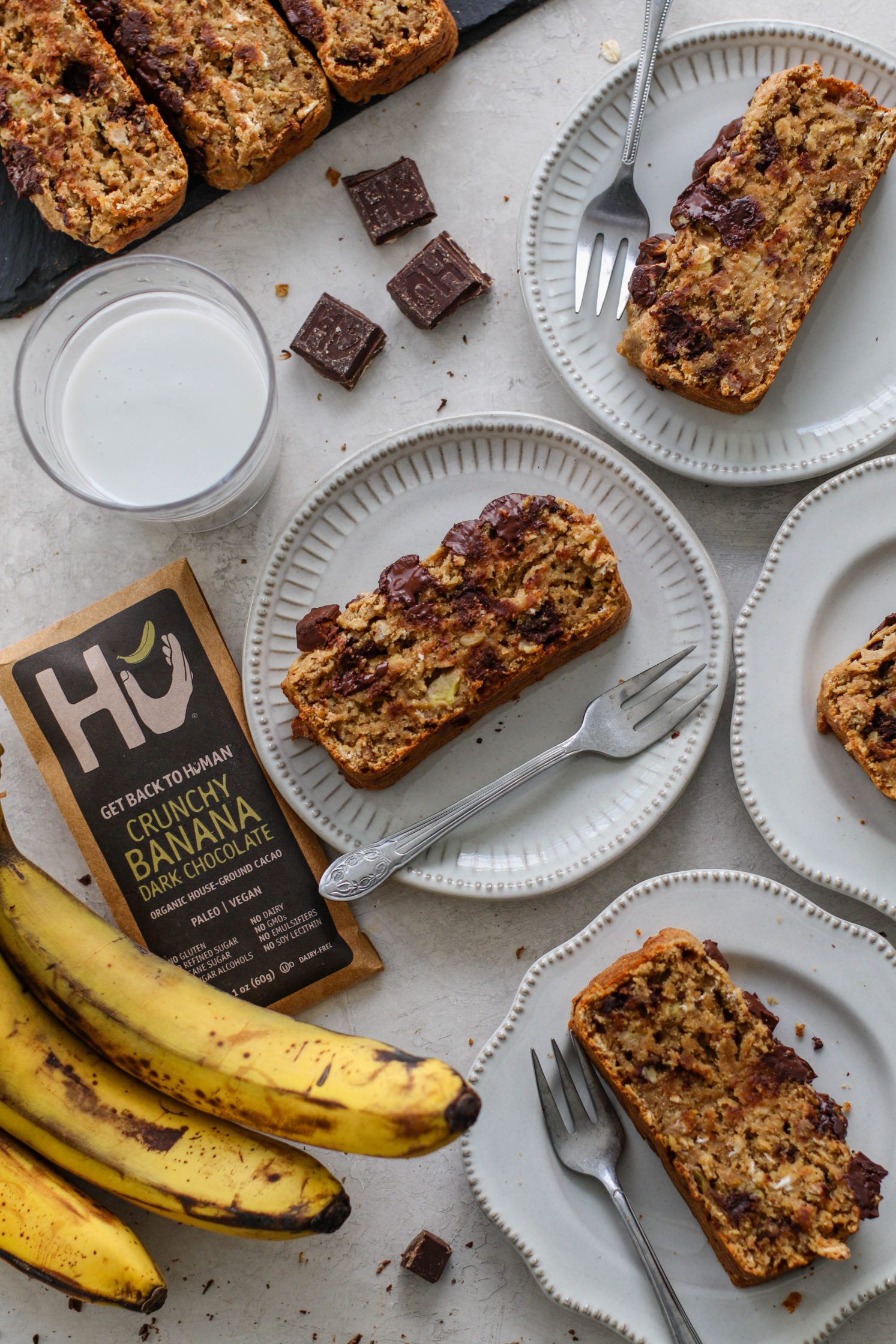 Vegan Banana Chocolate Chunk Bread served on white plates with forks with bananas and dark chocolate pieces with glass of milk