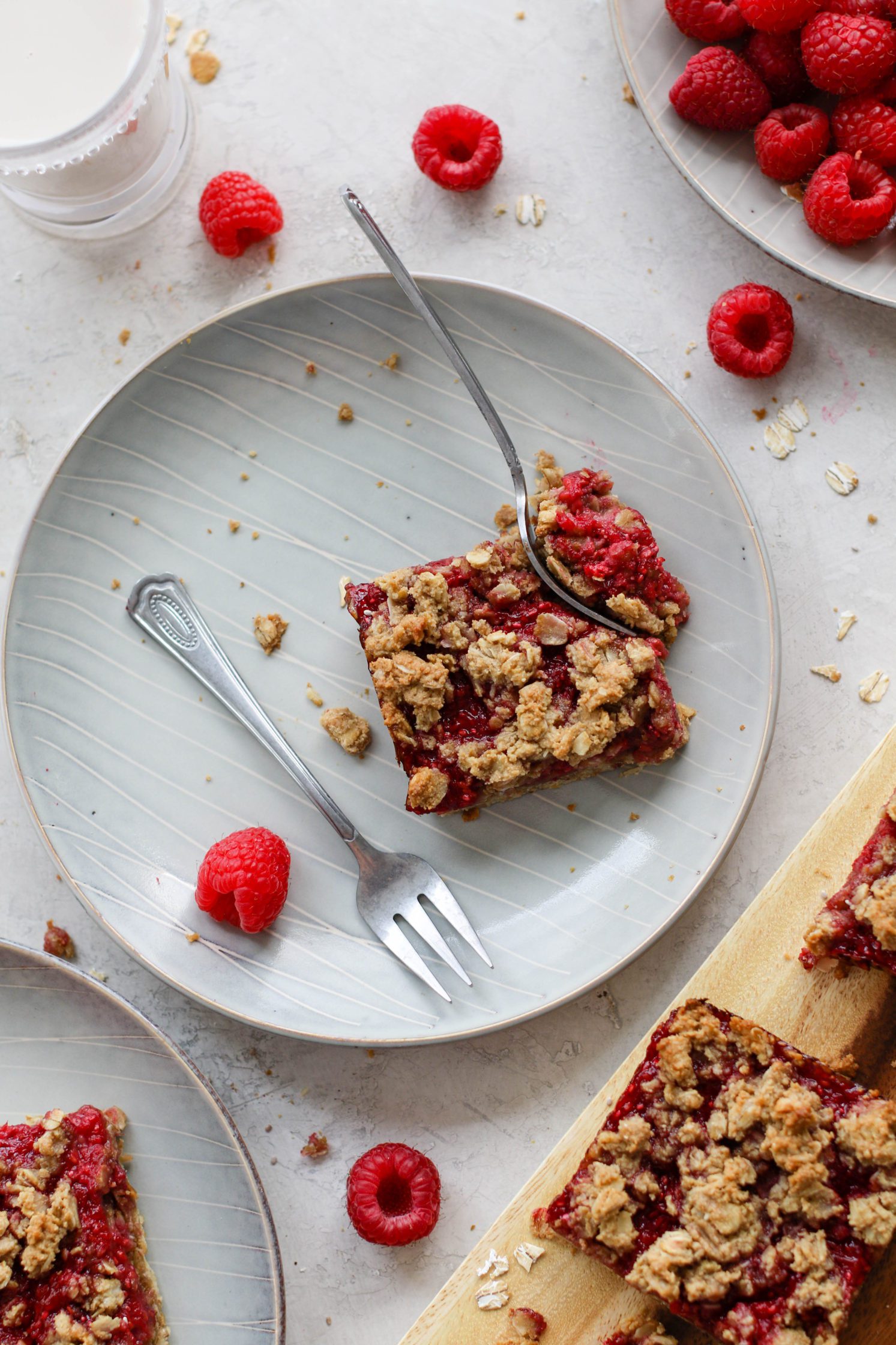 Raspberry Oat Crumble Bar served on plate with fork taking piece out and raspberries scattered by Flora & Vino