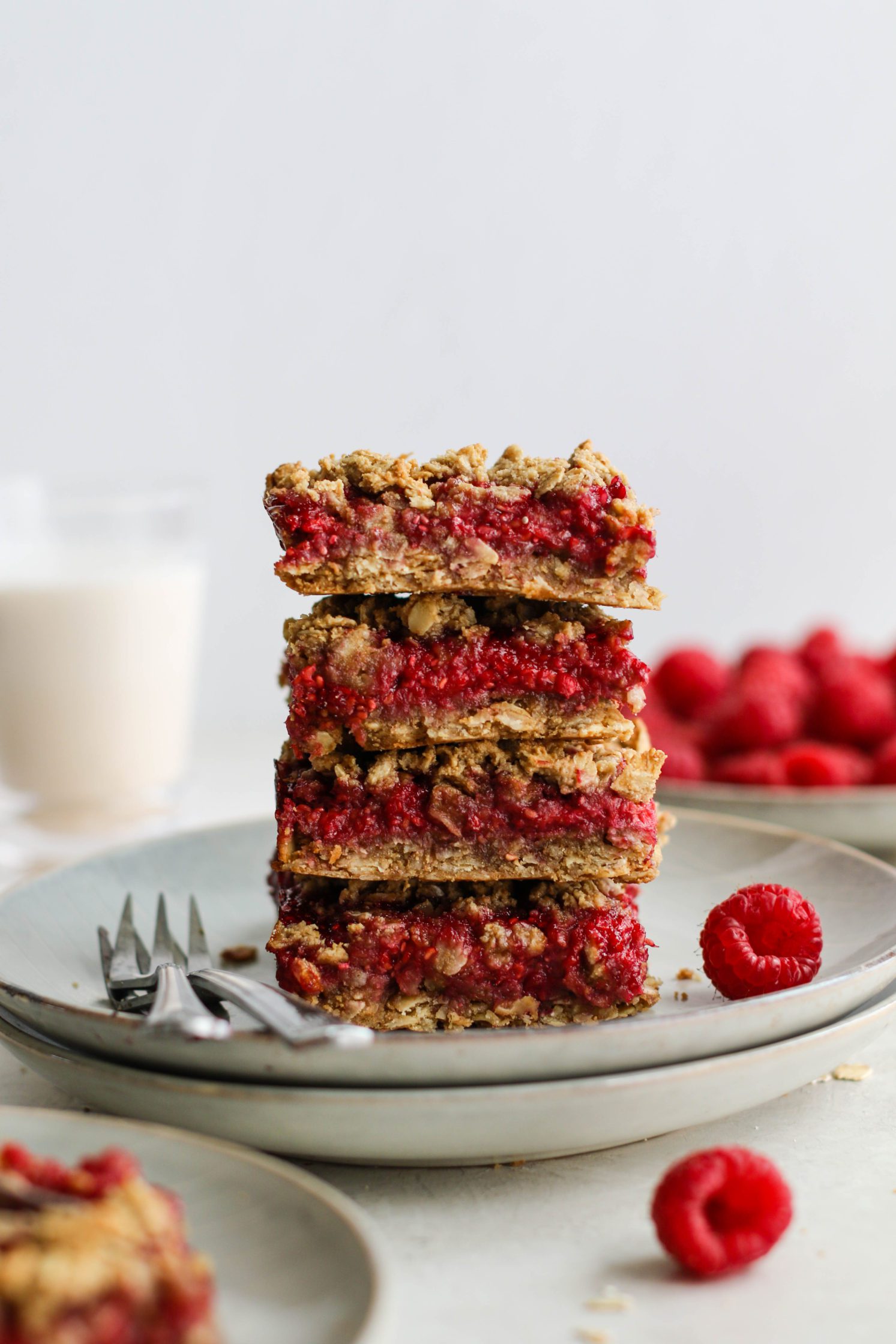 Raspberry Oat Crumble Bars stacked on plates with two forks and raspberries by Flora & Vino