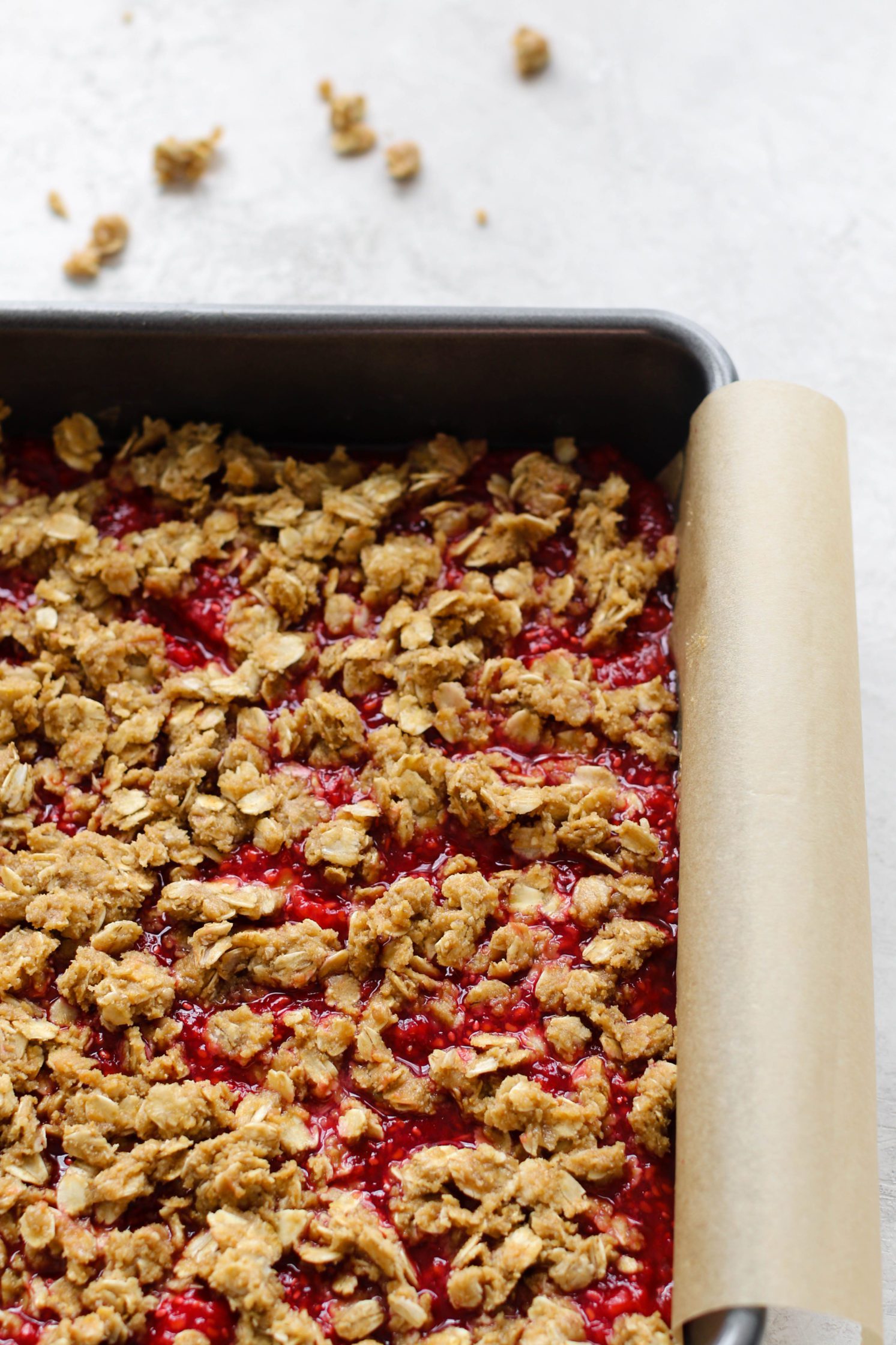 Raspberry Oat Crumble Bars unbaked in parchment lined baking pan by Flora & Vino