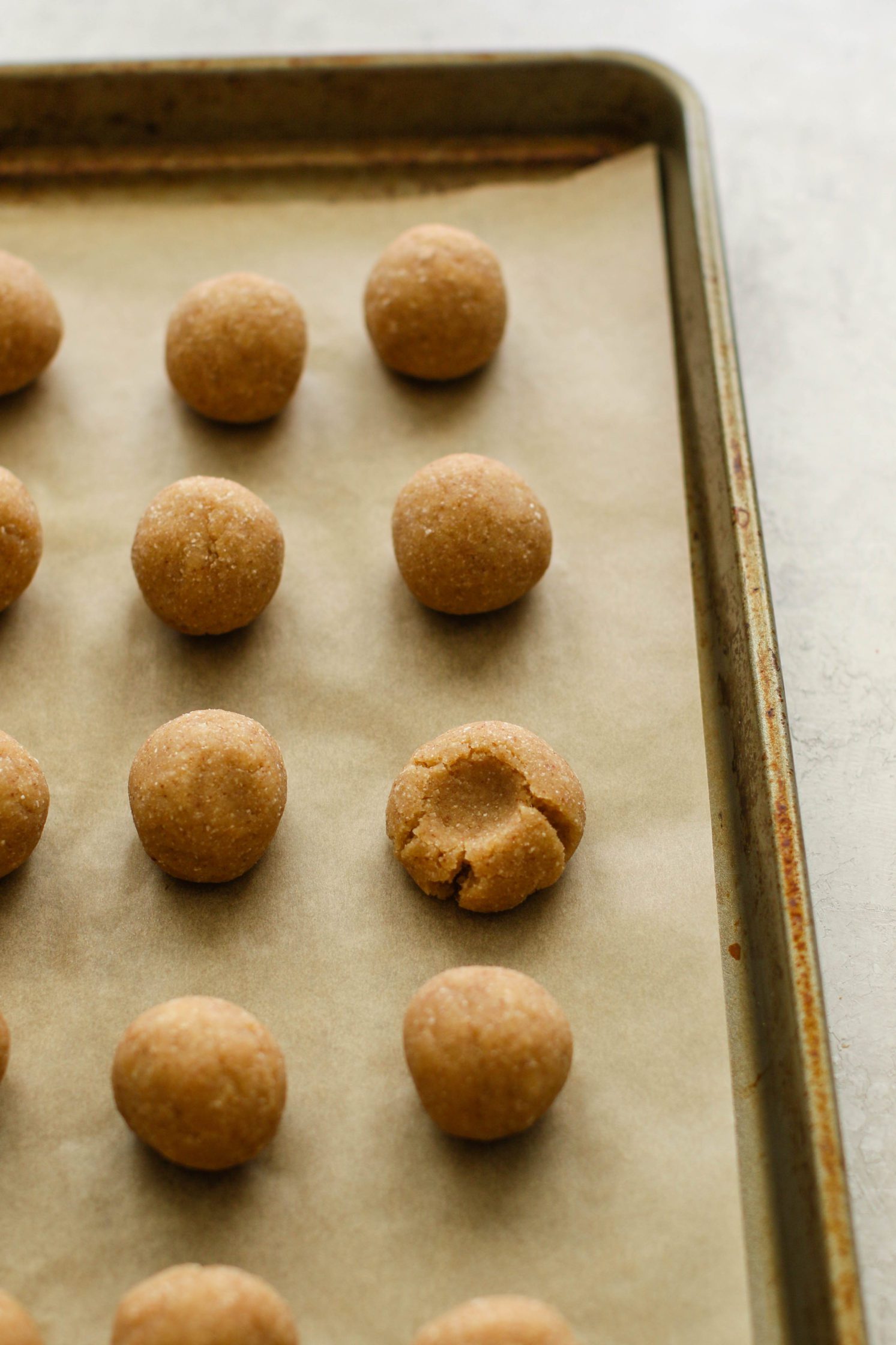 Coconut Caramel Thumbprint Cookies in balls on parchment lined baking sheet with thumb indenting one by Flora & Vino 