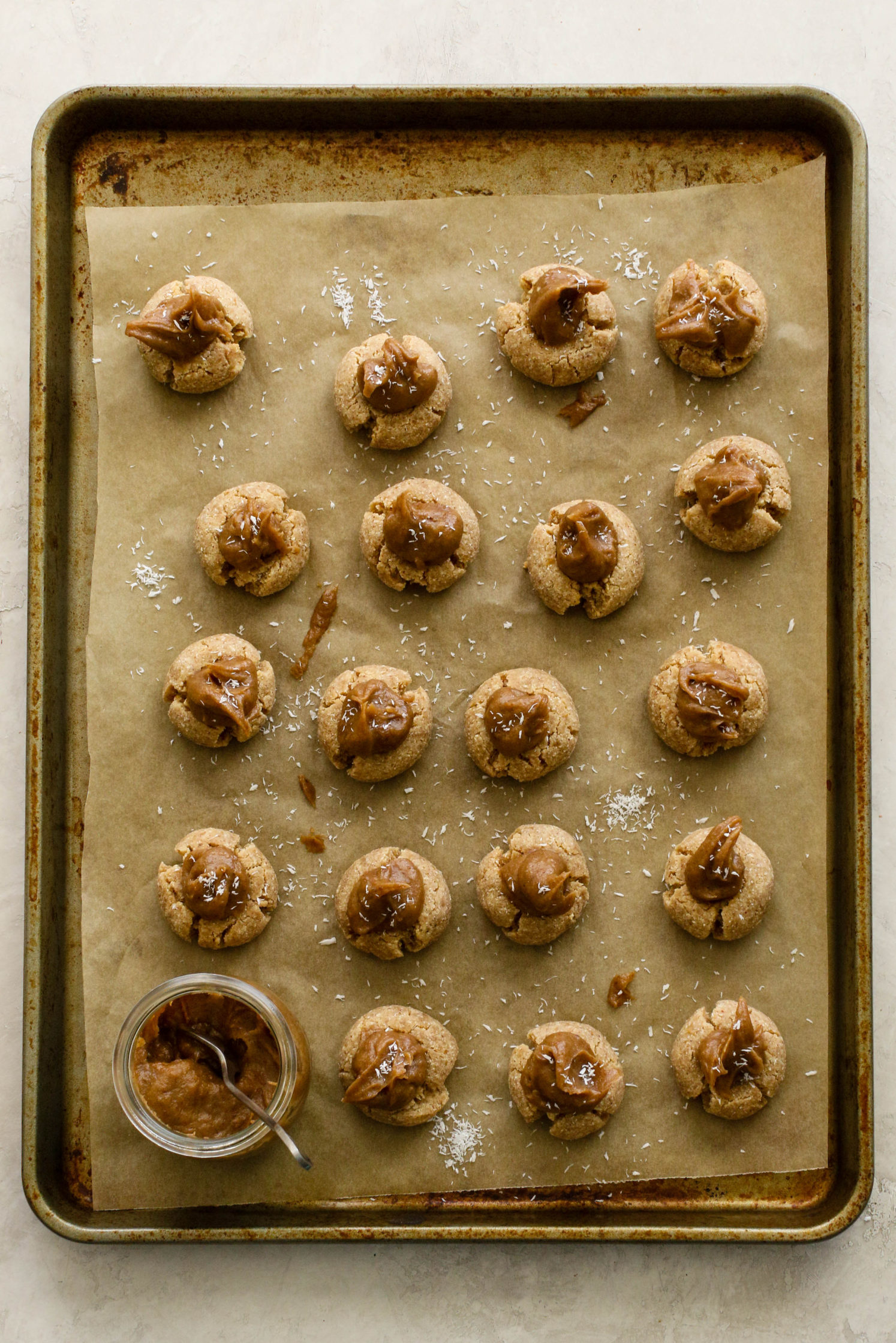 Coconut Caramel Thumbprint Cookies with date caramel on parchment lined baking sheet by Flora & Vino 