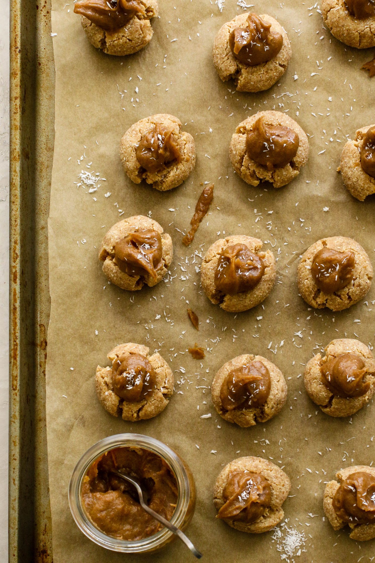 Coconut Caramel Thumbprint Cookies on parchment lined baking sheet with date caramel by Flora & Vino 