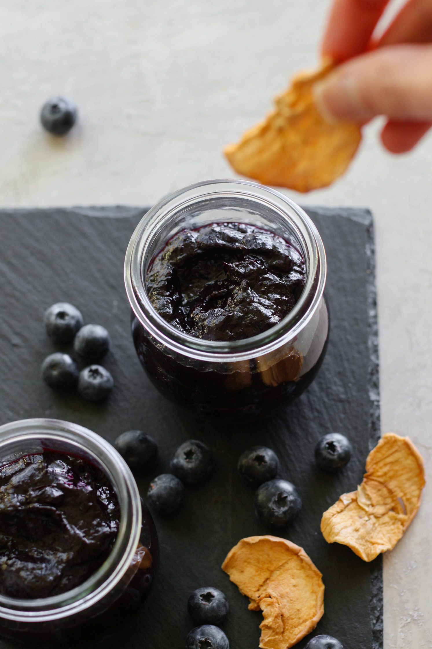hand dipping apple chips in Blueberry Butter (No-Sugar-Added) by Flora & Vino 