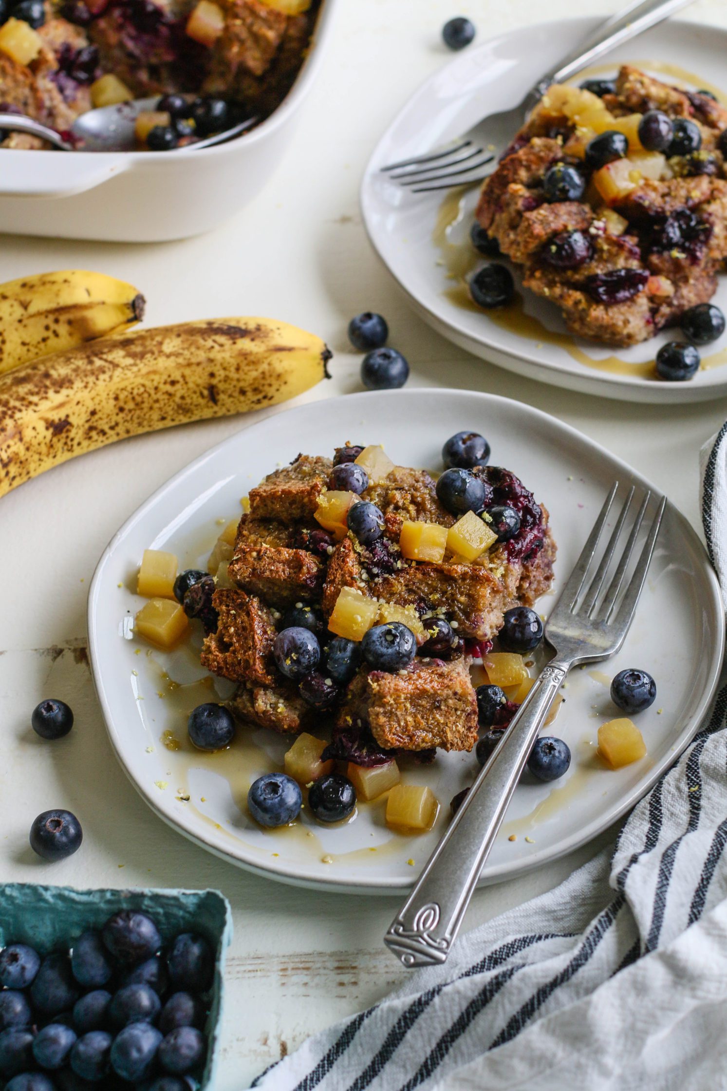 Banana Blueberry French Toast Casserole served on plates with a forks topped with fresh blueberries and golden beet