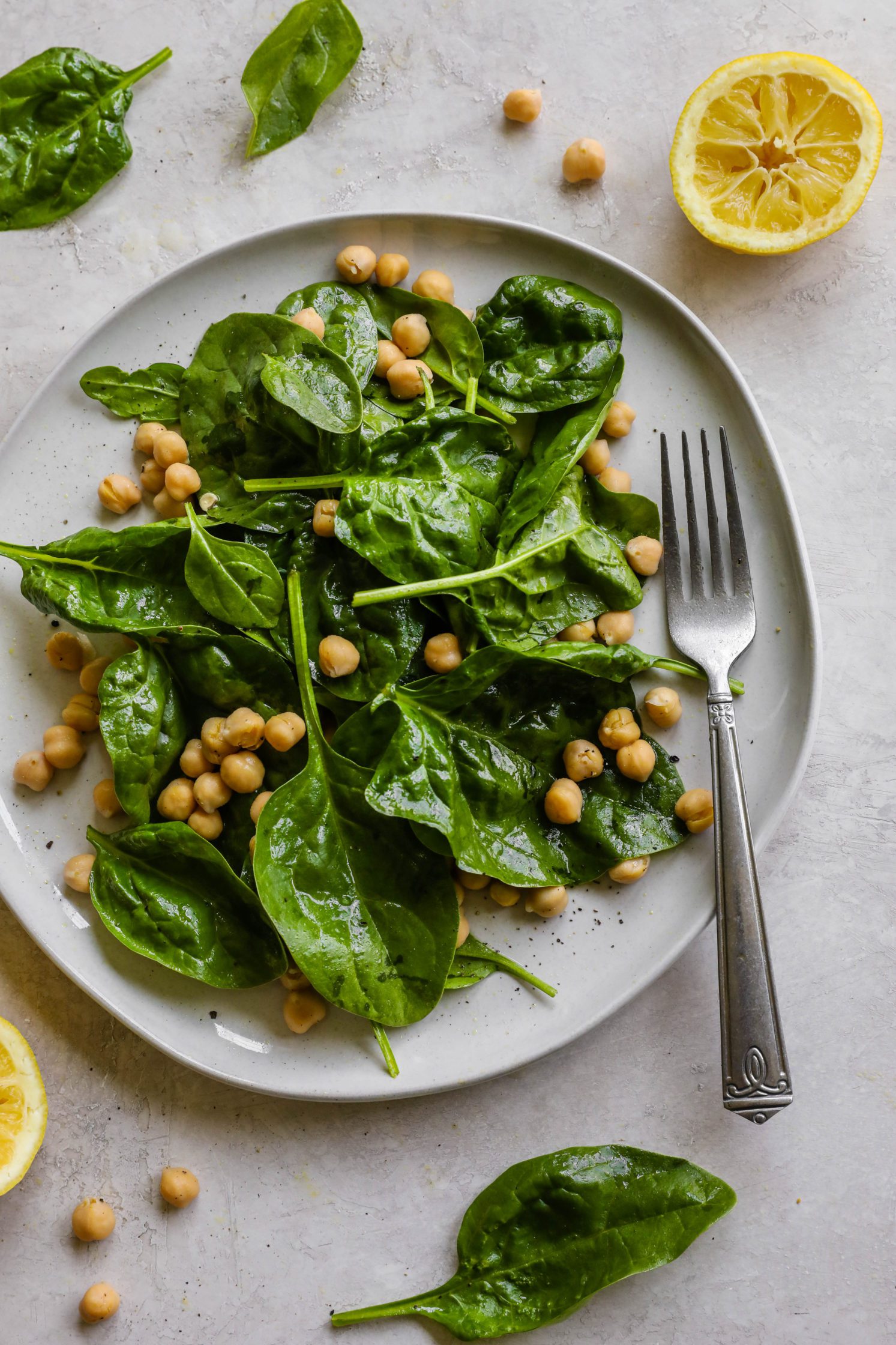 2-Minute Lemon, Spinach, & Chickpea Salad served on a plate with a fork with chickpeas and spinach and lemon on the side by Flora & Vino