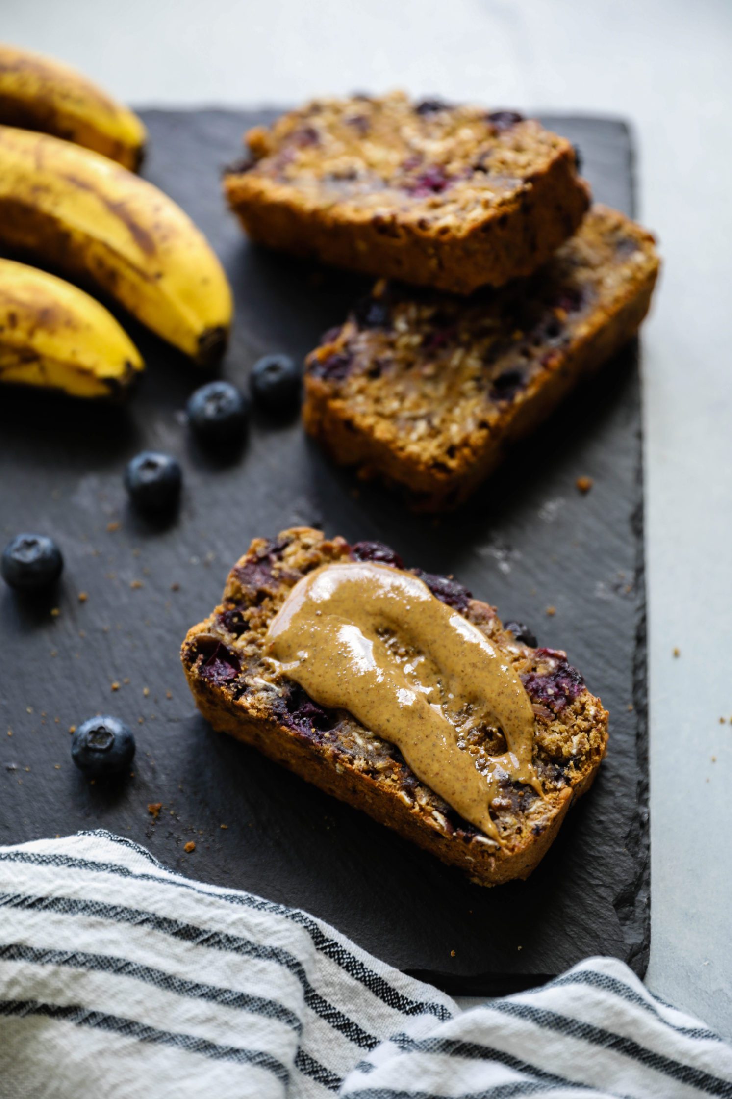Blueberry Banana Breakfast Bread sliced with smear of nut butter on one slice by Flora & Vino