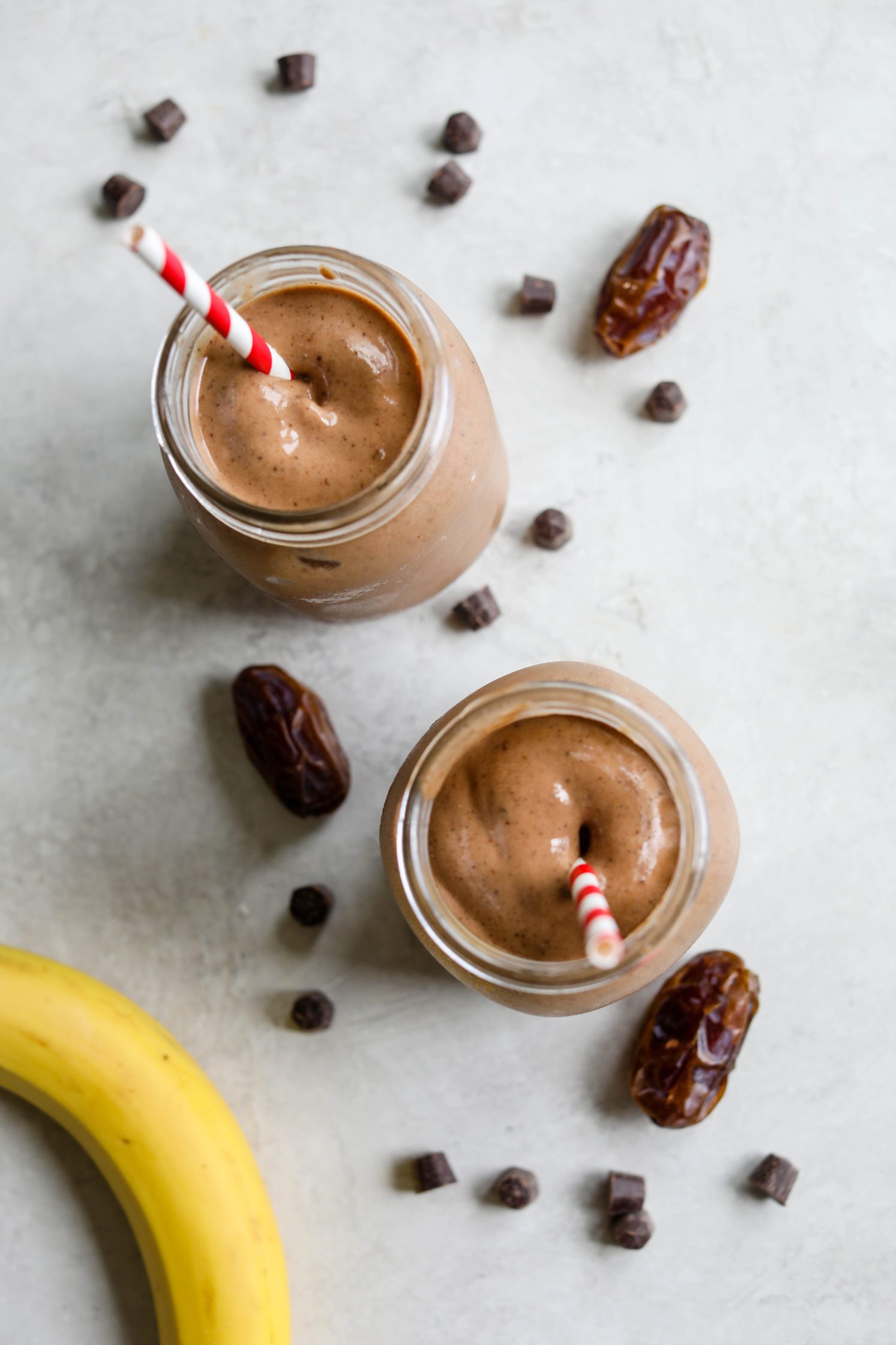 Healthy Vegan Chocolate Frosty served with red and white striped straws with dates, chocolate chips, and banana