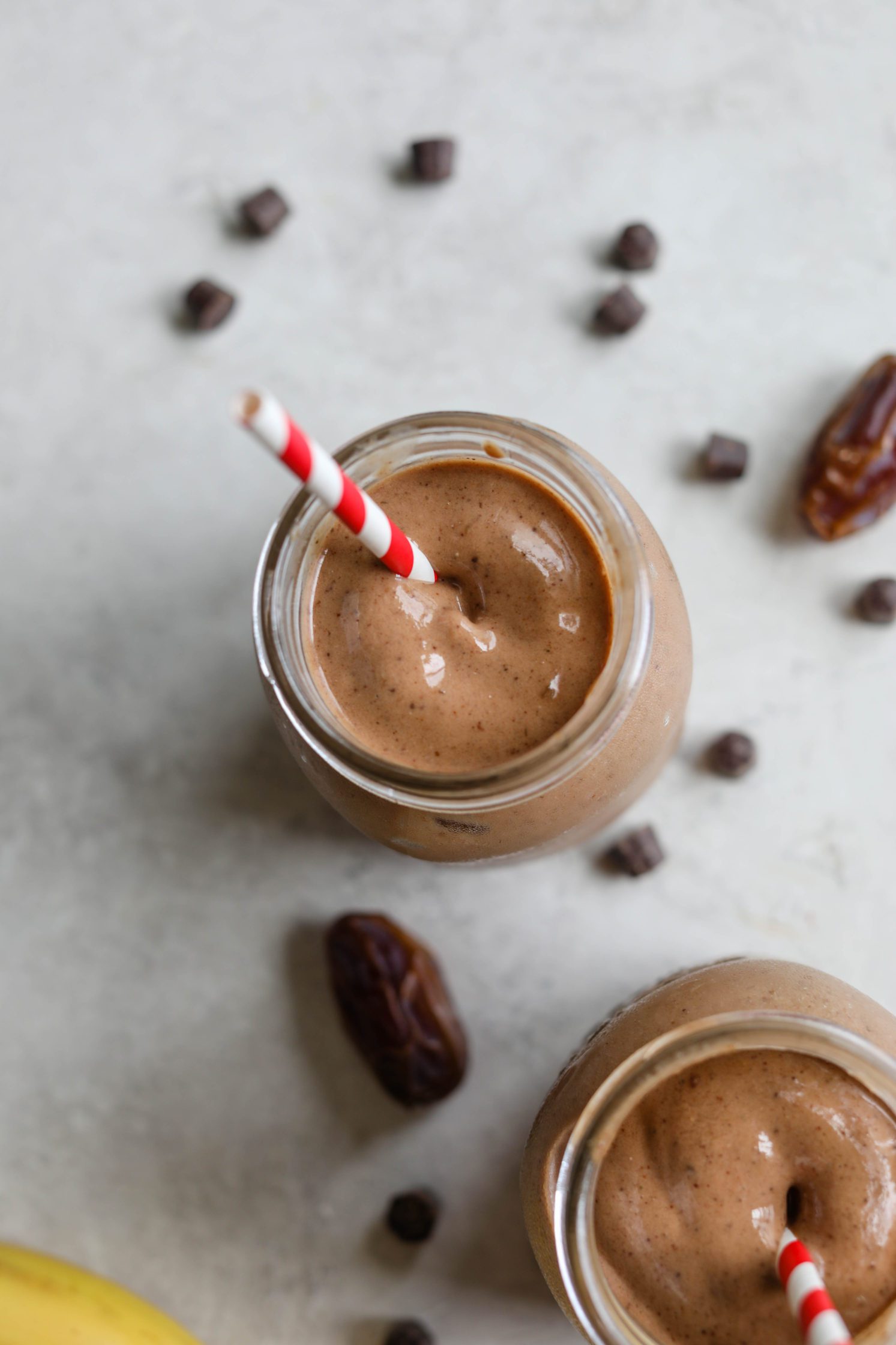 Healthy Vegan Chocolate Frosty served with red and white striped straws with dates, chocolate chips, and banana