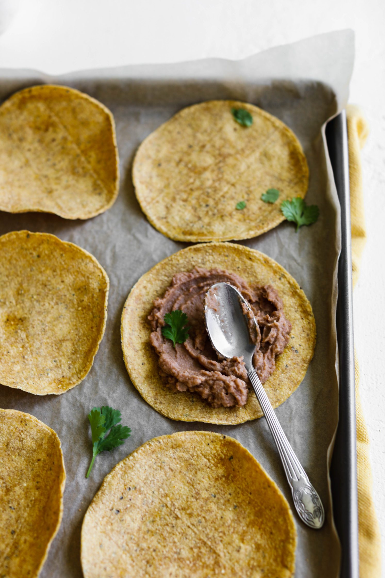 spoon spreading refried beans on baked tortilla with spoon