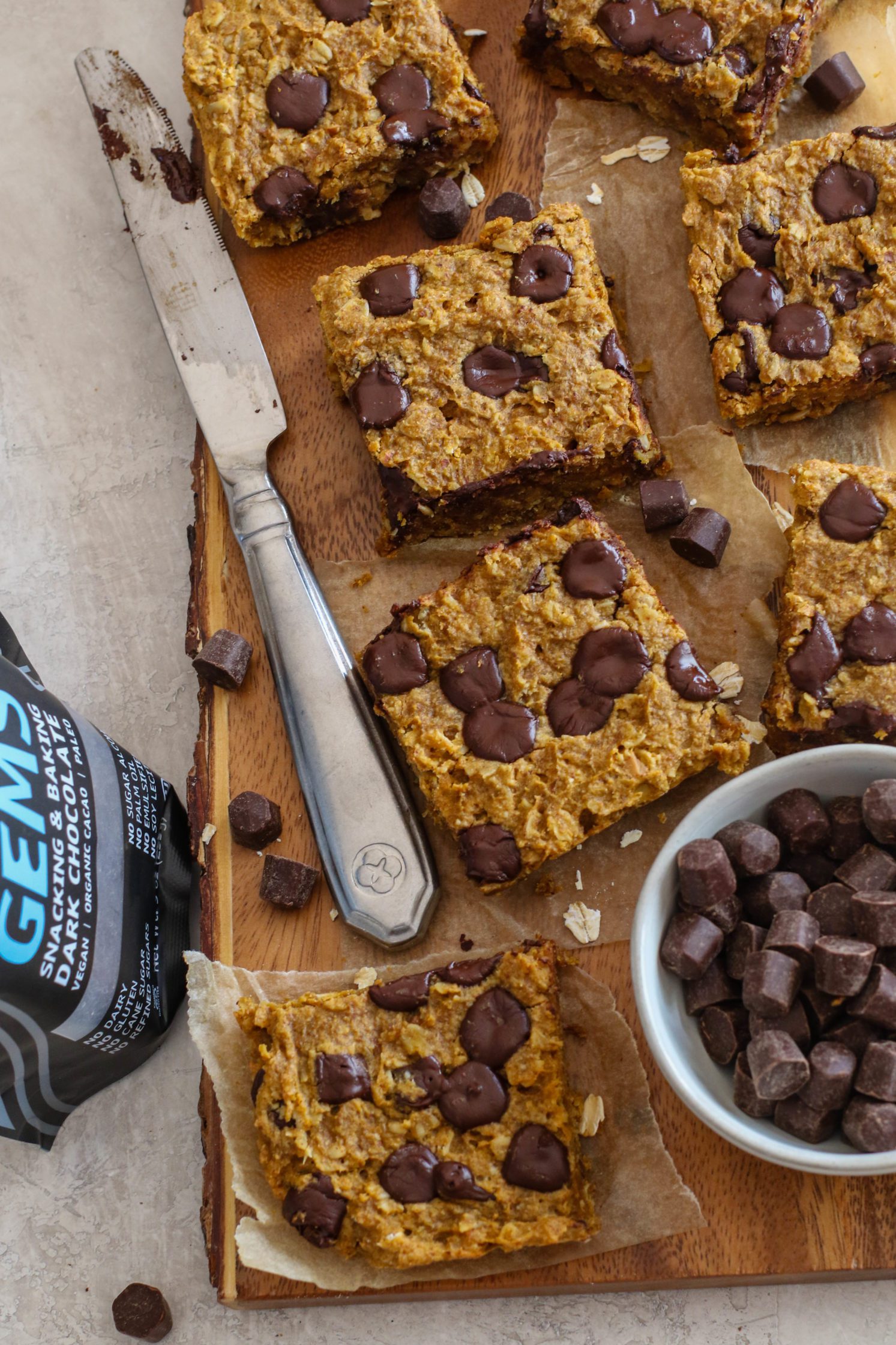 Pumpkin Chocolate Chip Breakfast Bars served on parchment paper on wooden board with chocolate and oats scattered 