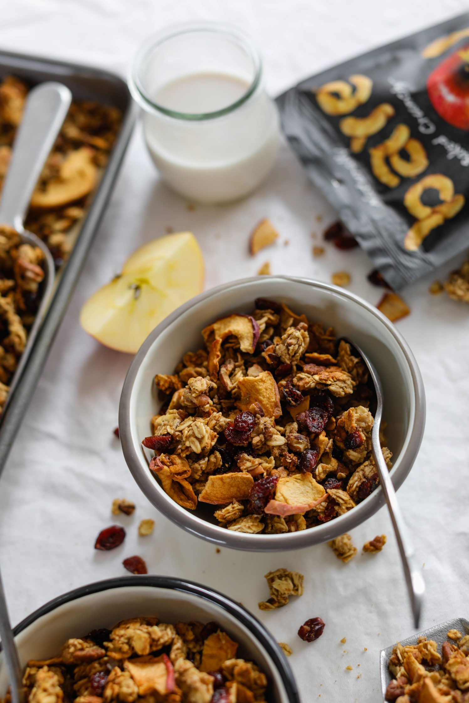 Apple Cranberry Pecan Granola served in bowls with spoons and glass of almond milk with baking sheet 