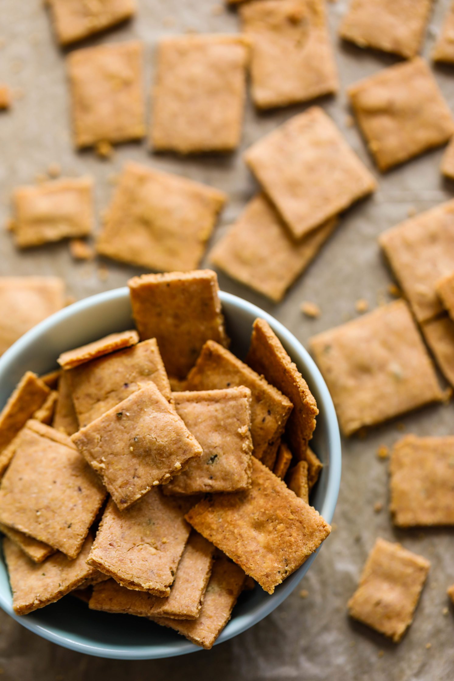 Grain-Free Almond Flour Crackers on parchment lined baking sheet with bowl of crackers on bottom
