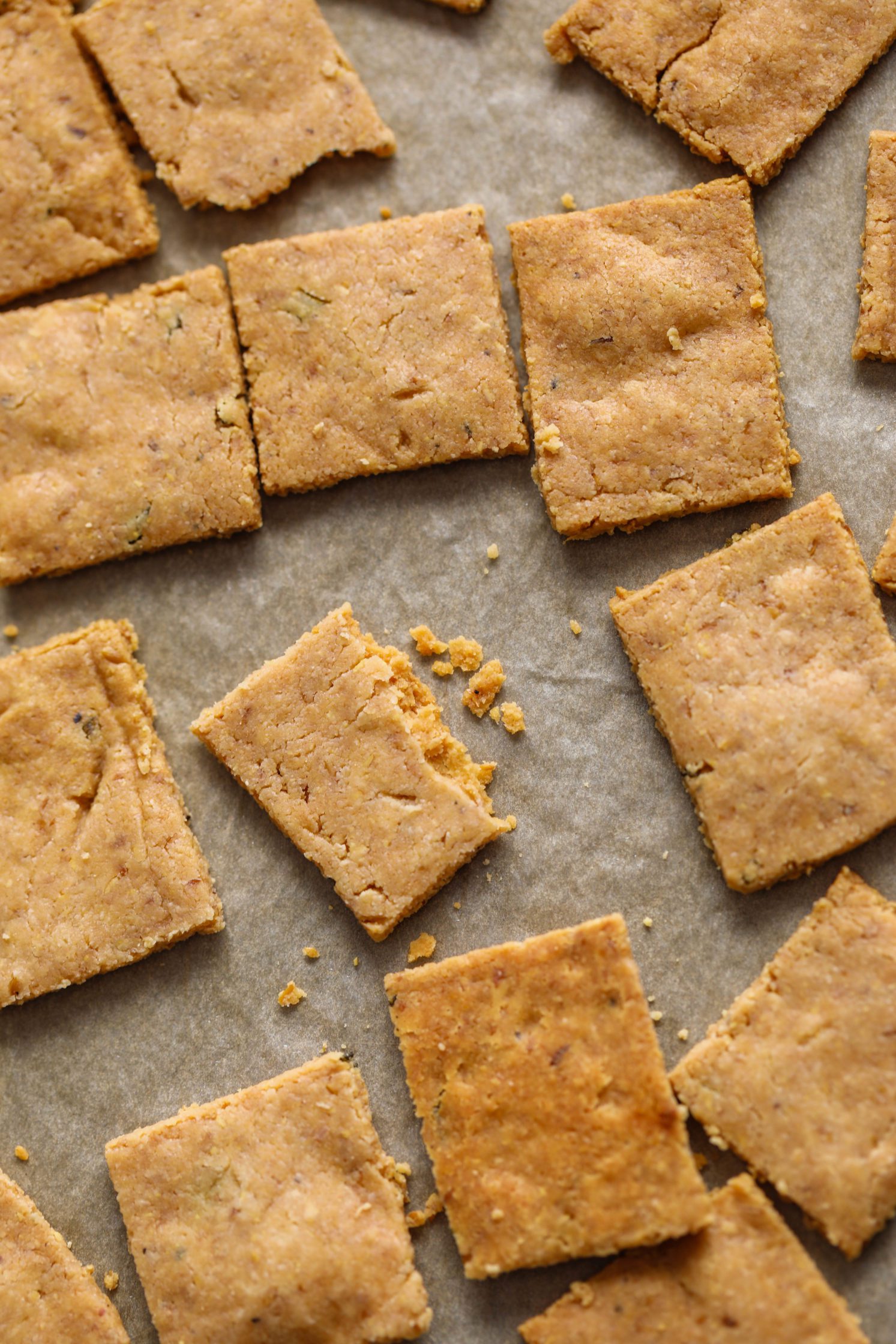 Grain-Free Almond Flour Crackers on parchment lined baking sheet with bowl of crackers on bottom