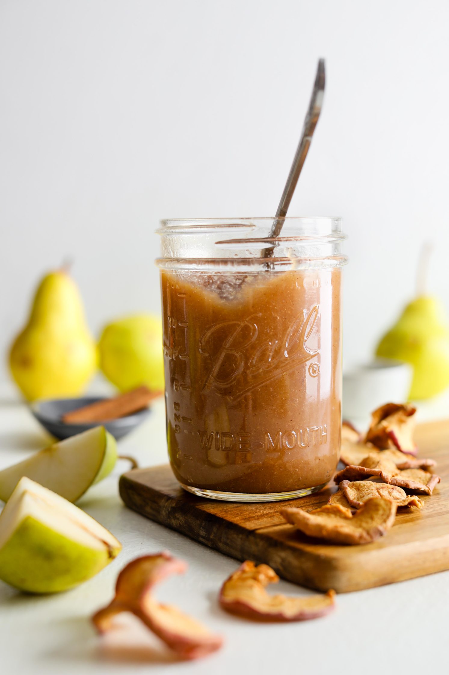 Maple Pear Butter served in mason jar with a spoon surrounded by apple chips by Flora & Vino