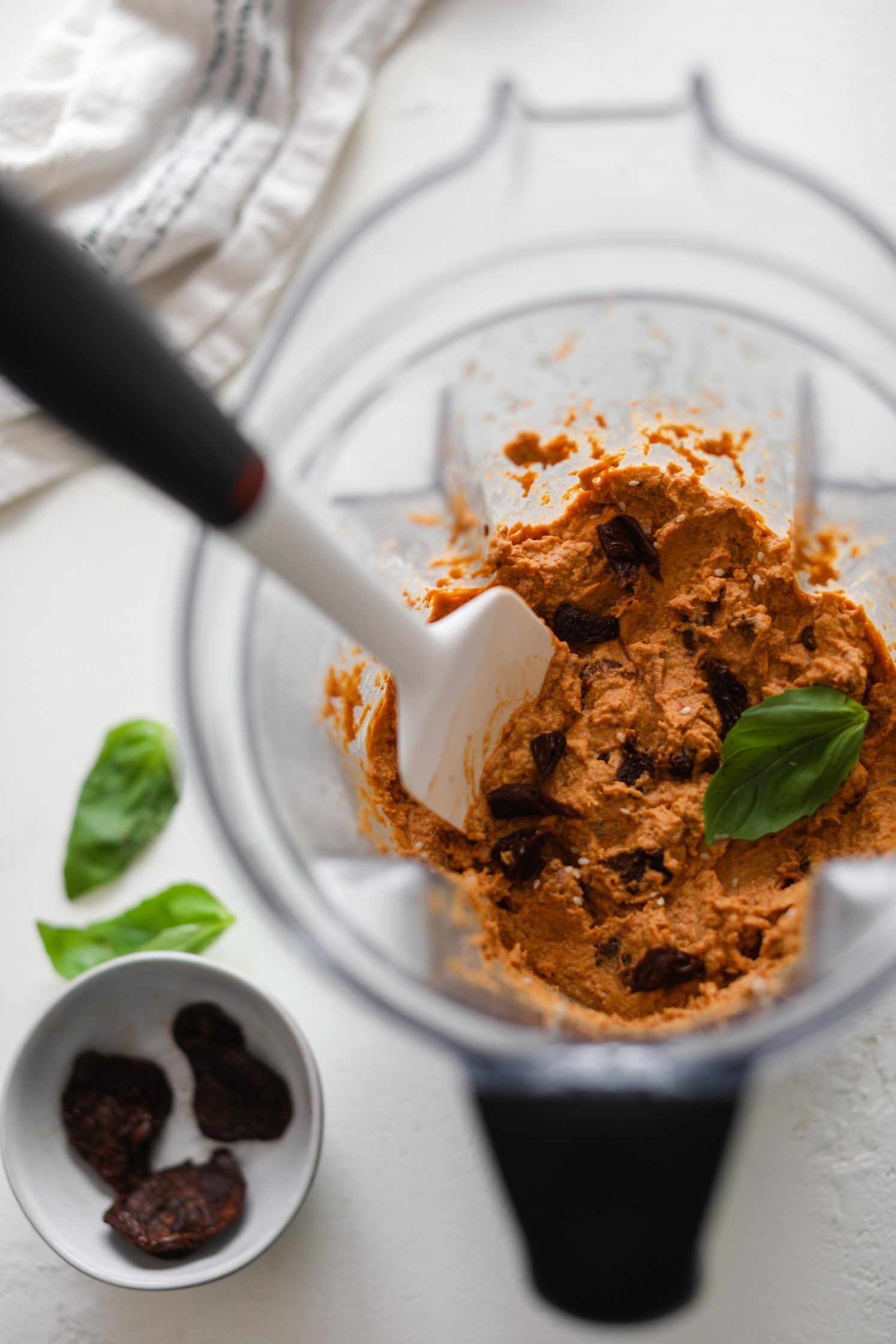 Sun-Dried Tomato Hummus blended in blender with fresh basil leaves and spatula