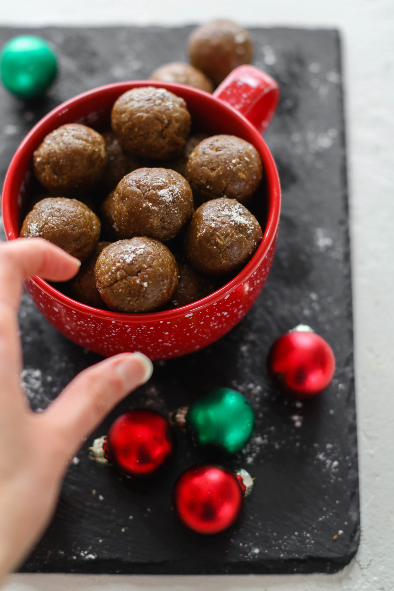 hand reaching for Gingerbread Bliss Balls in red mug by Flora & Vino 