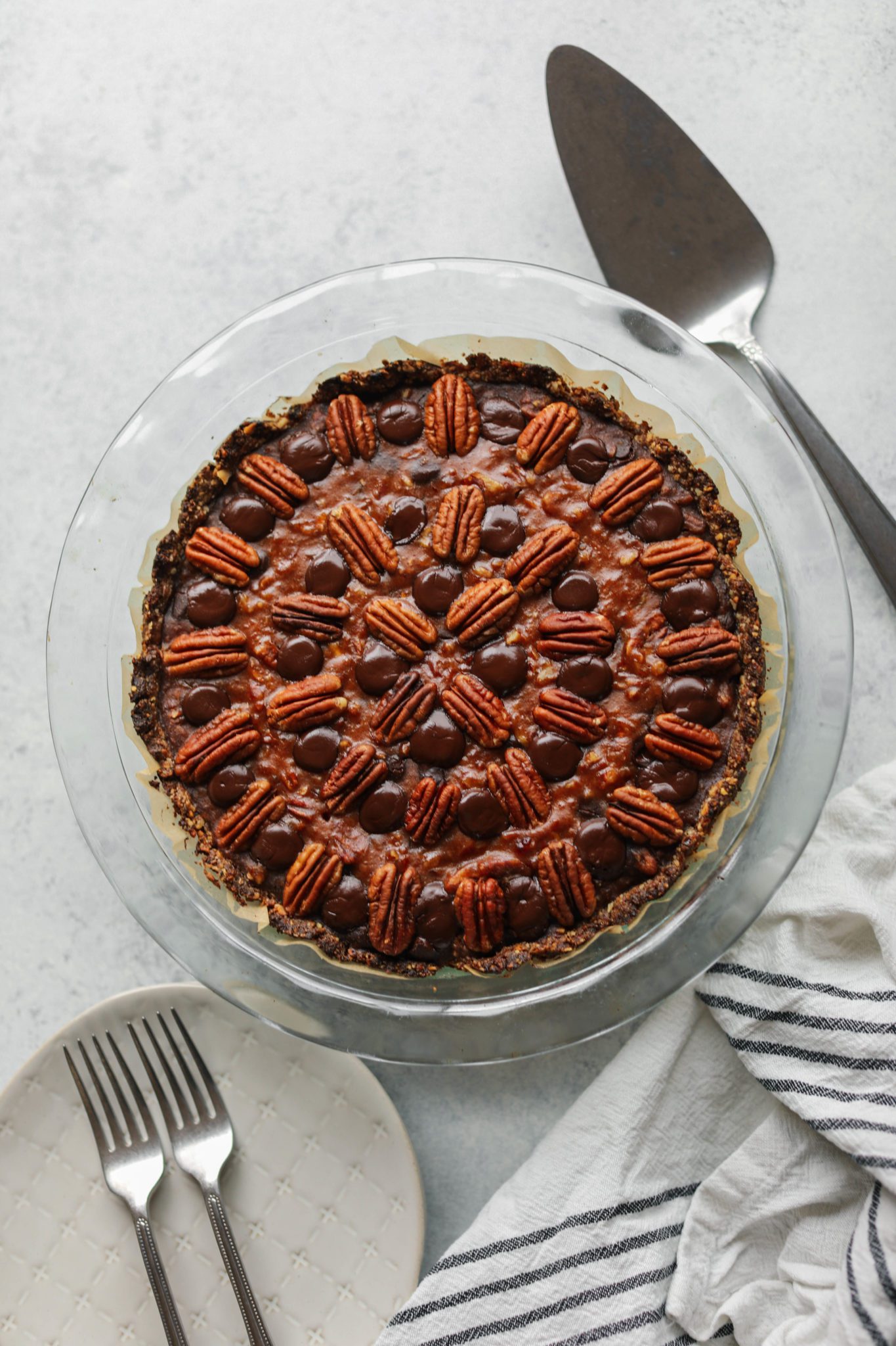 Vegan Dark Chocolate Pecan Pie baked in pie pie with pie server and plates and forks by Flora & vino