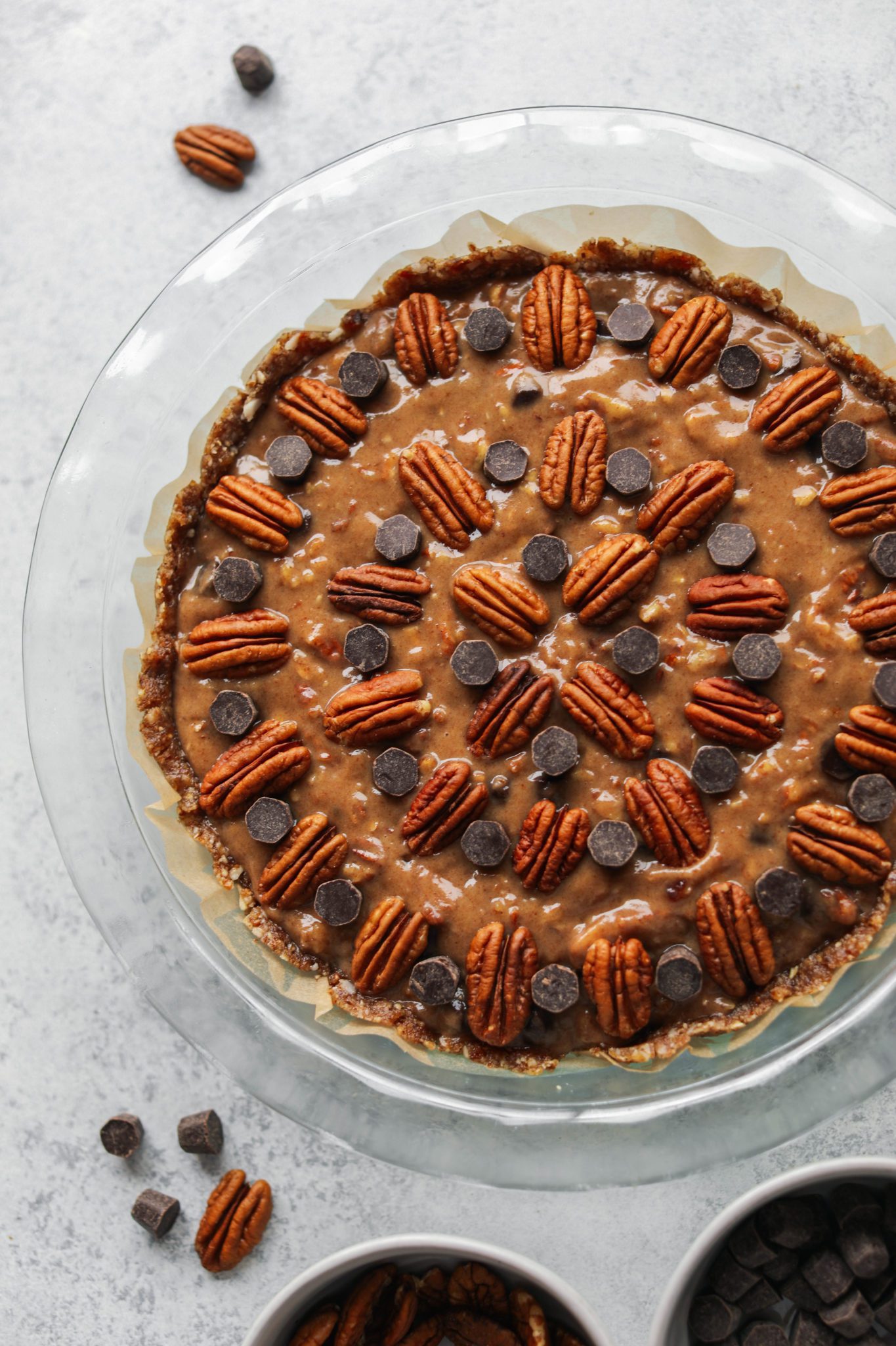 Pecan Pie filling topped with dark chocolate chips and pecans in pie pan by Flora & vino