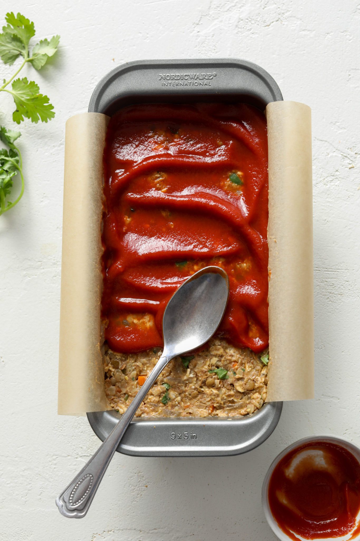 Vegan Lentil Oat Loaf in parchment lined baking pan topped with ketchup by Flora & Vino 