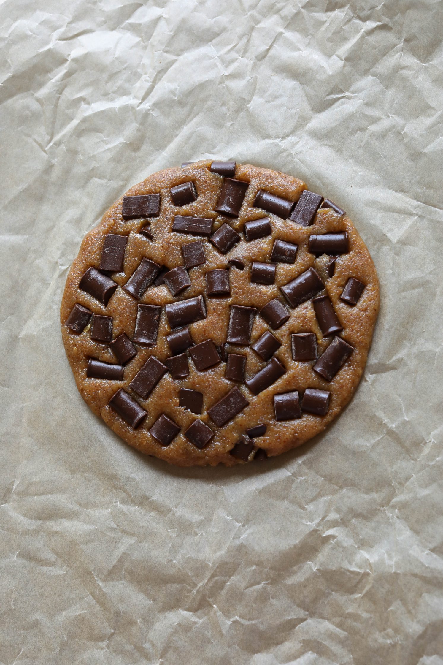 Giant Almond Flour Chocolate Chip Cookie molded into circle on parchment paper by Flora & Vino 