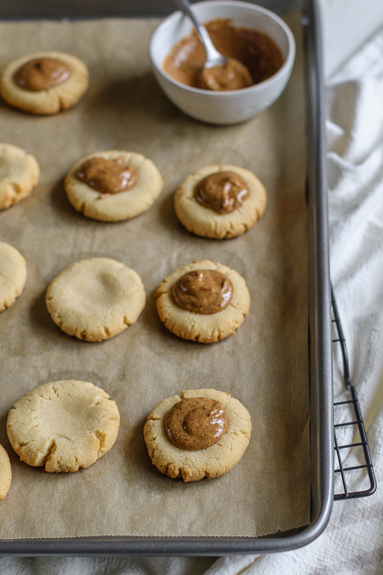 Vegan Almond Butter Tagalongs baked on parchment lined baking sheet with dollop of almond butter in the center and bowl of almond butter