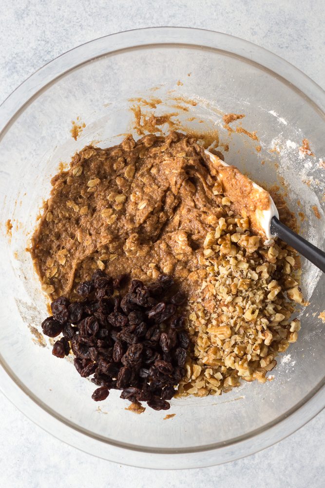 Apple Butter Oatmeal Cookie batter mixed in bowl with raisins and walnuts added on top with spatula