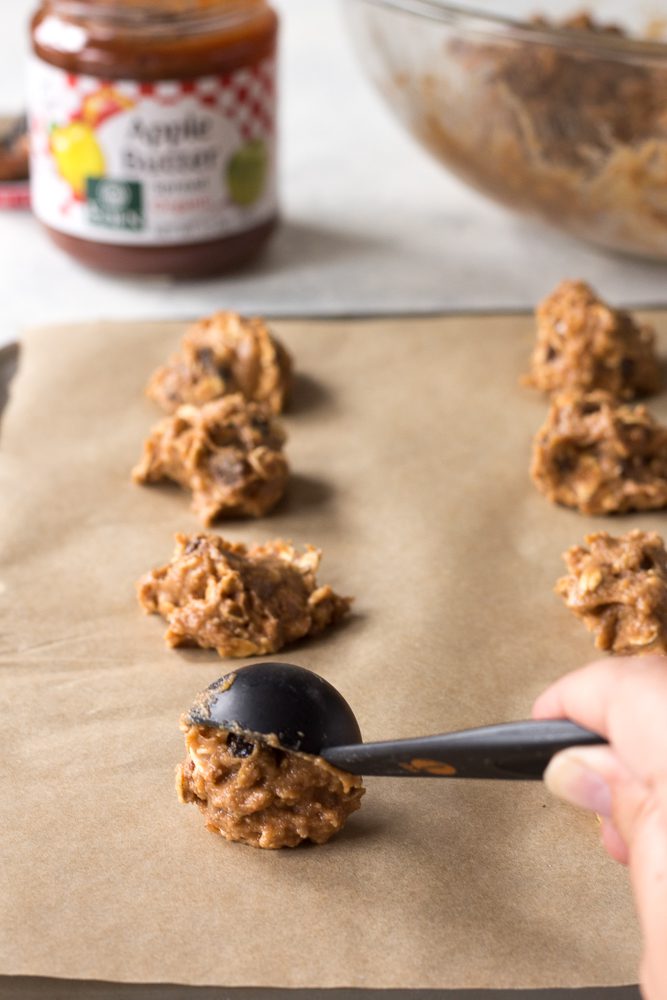 spooning apple butter oatmeal cookie batter onto parchment lined baking sheet