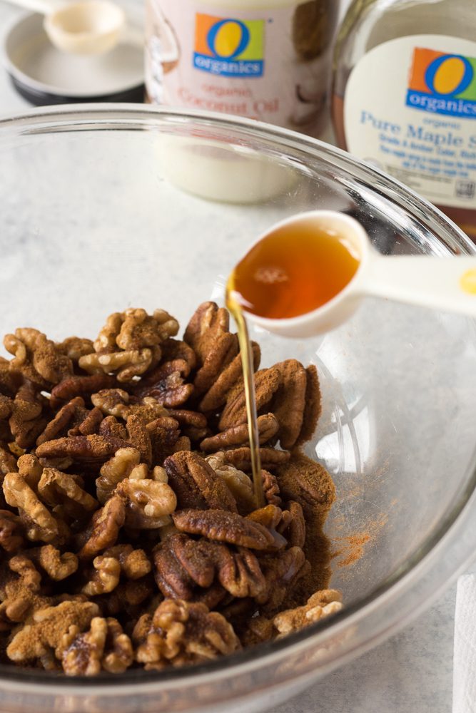 pouring maple syrup on mixed nuts in a bowl by Flora & Vino