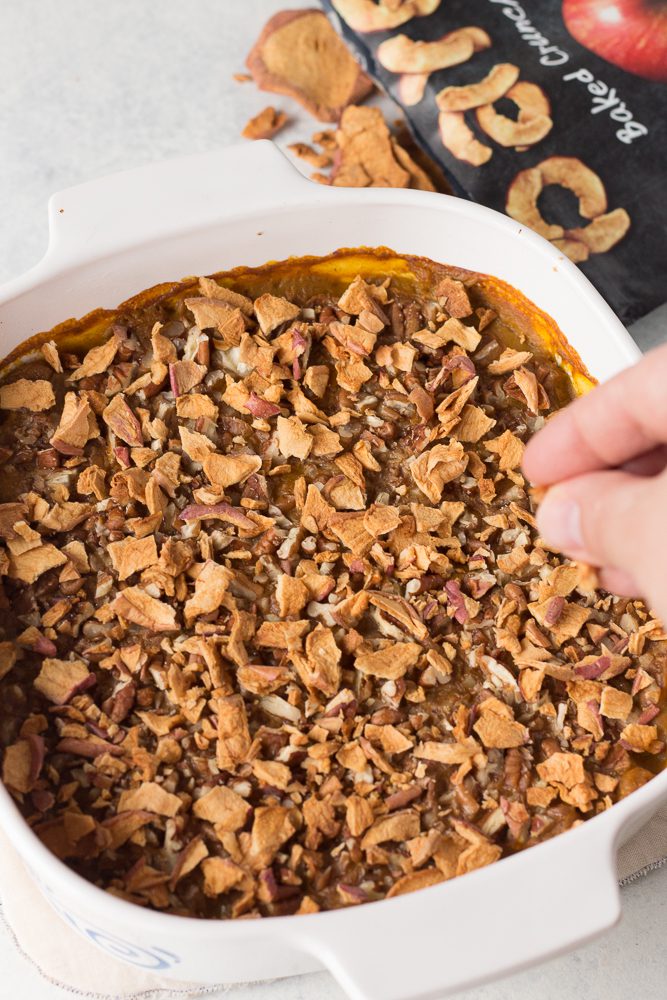 hand sprinkling apple chips on Pumpkin Apple Bake served in casserole dish  