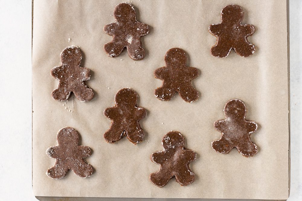 Vegan & Gluten-Free Gingerbread Cookies cut into shapes on parchment lined baking sheet by Flora & Vino 