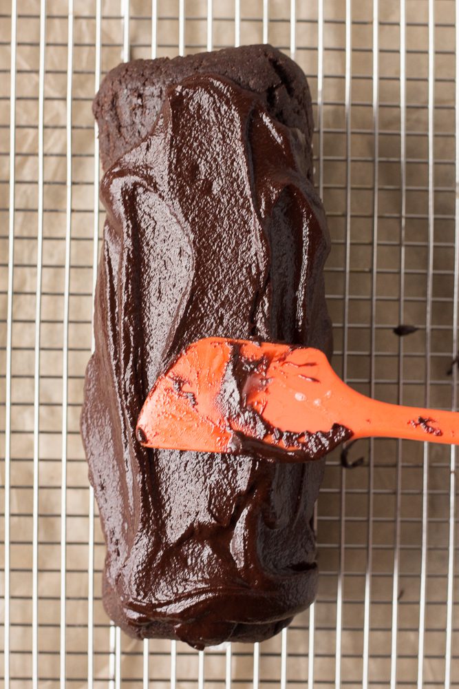 Vegan Dark Chocolate Swiss Roll topped with chocolate ganache with spatula by Flora & Vino