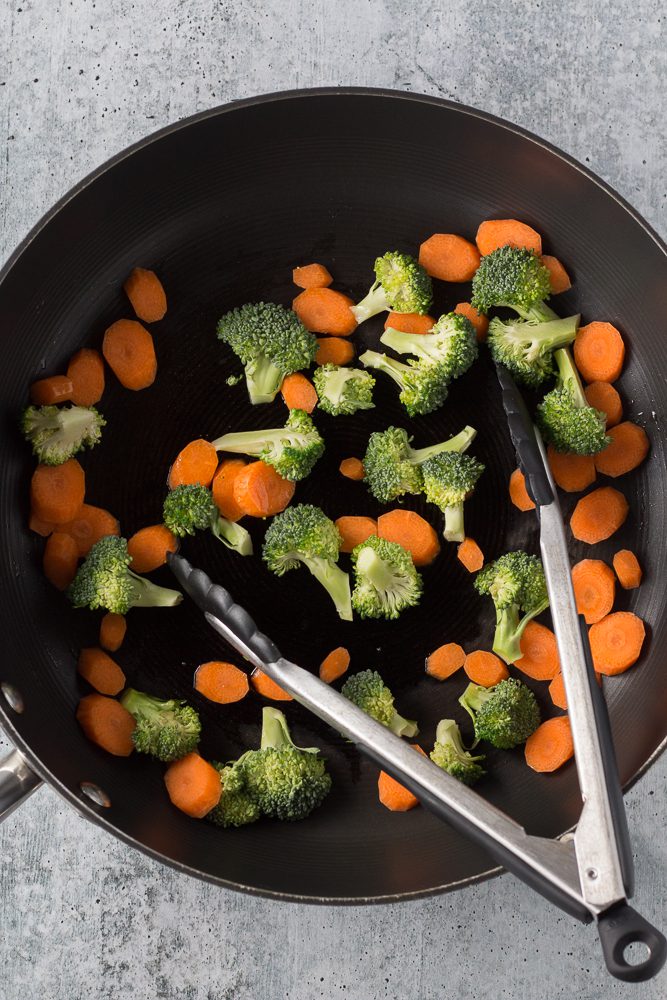 broccoli and carrots stir-fried in pan with tongs by Flora & Vino
