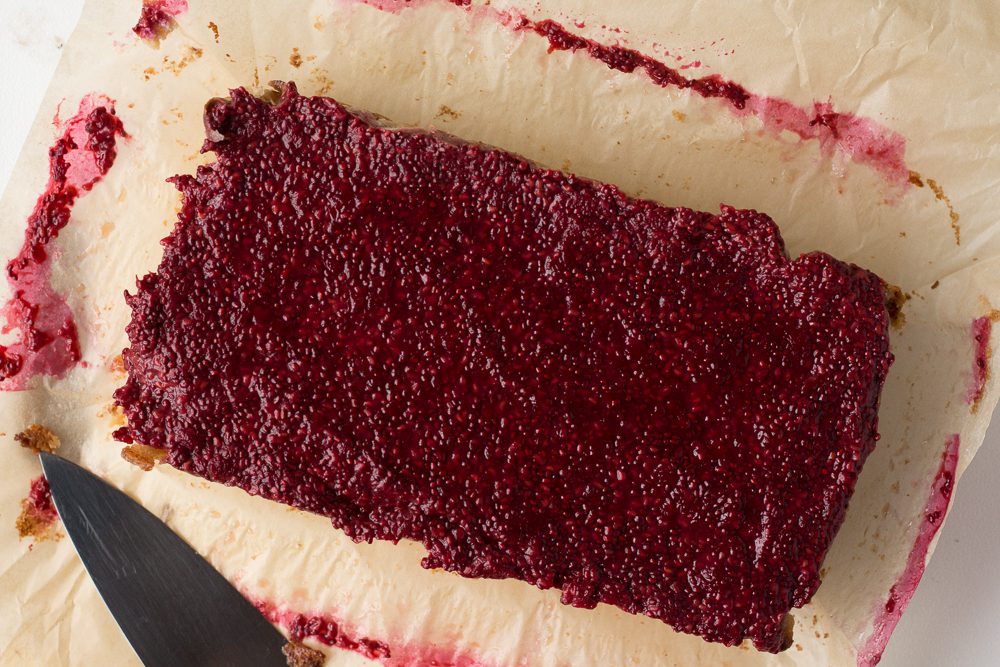 Vegan Raspberry Cheesecake cooled on parchment paper with a knife on the side by Flora & Vino 