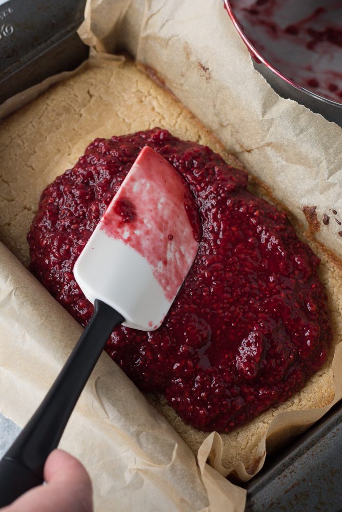 raspberry filling spread on top of baked vegan cheesecake with a spatula by Flora & Vino 