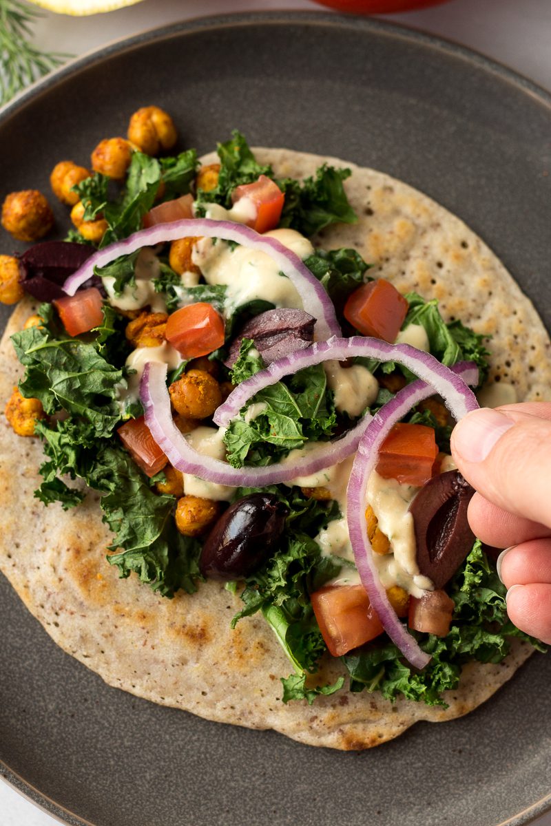 hand assembling ingredients on grain free flatbread wrap on gray plate