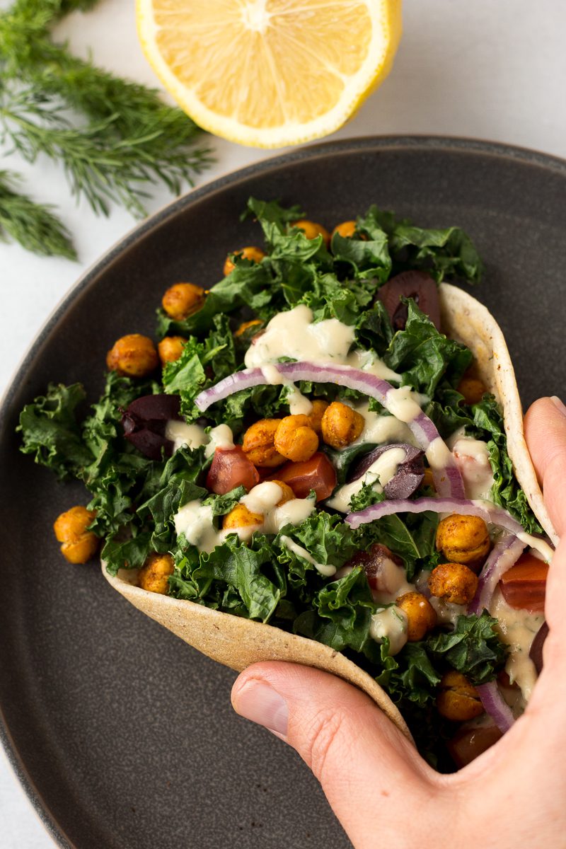 hand holding Grain-Free Flatbread Wraps with Tandoori Chickpeas on gray plate with dill and lemon on side