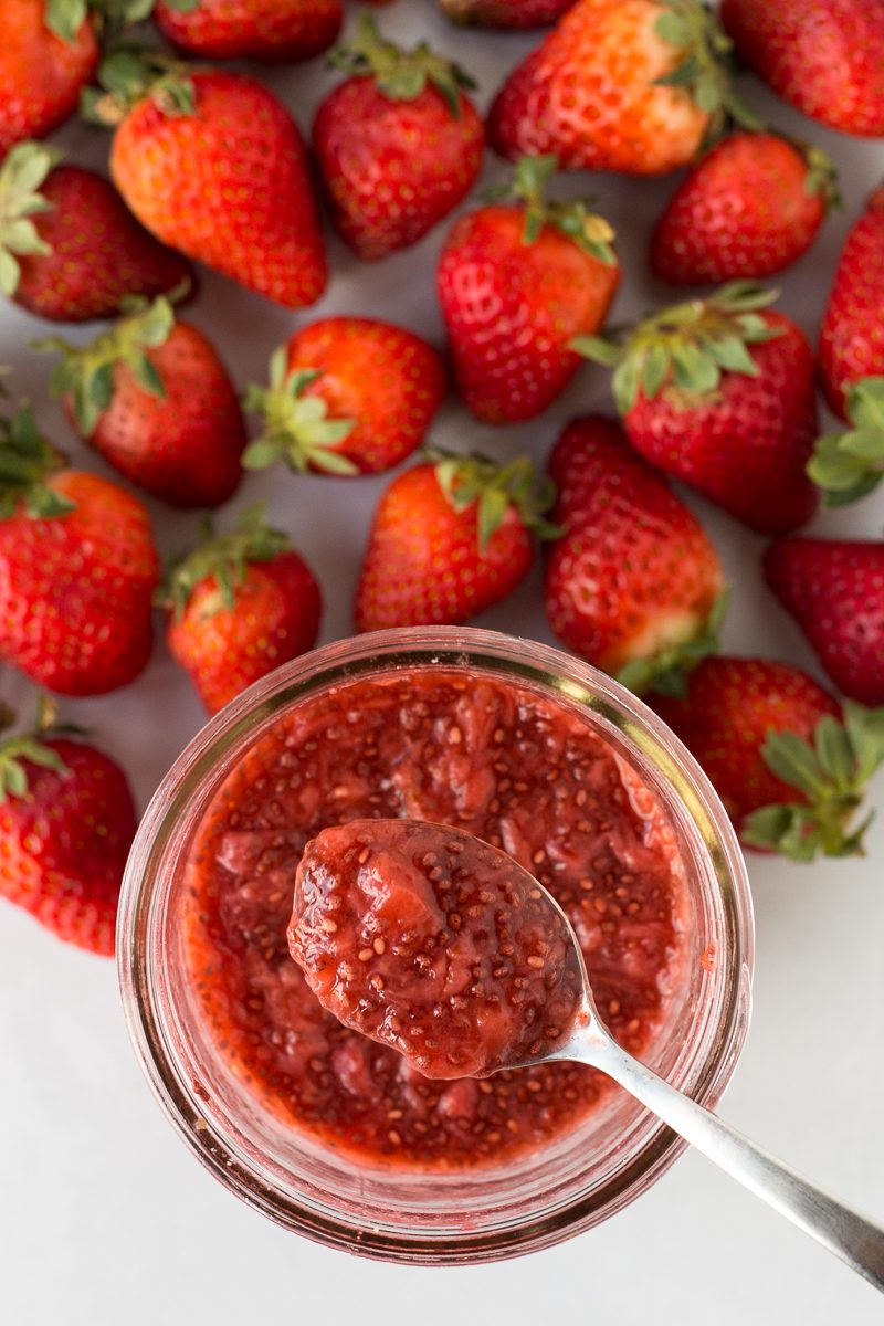 Strawberry Chia Seed Jam served in mason jar with a spoon surrounded by fresh strawberries
