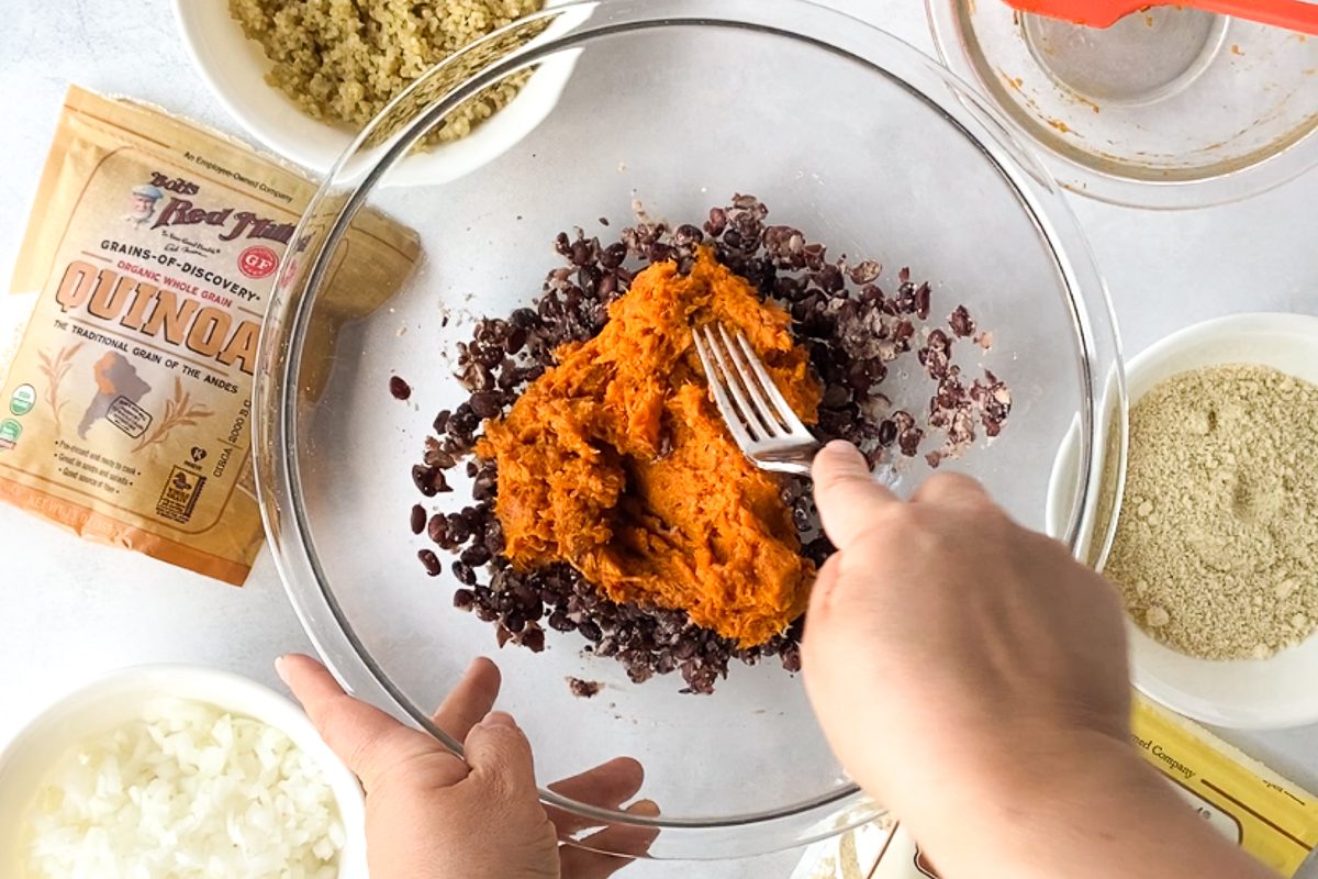 hand smashing sweet potato and black beans together in bowl