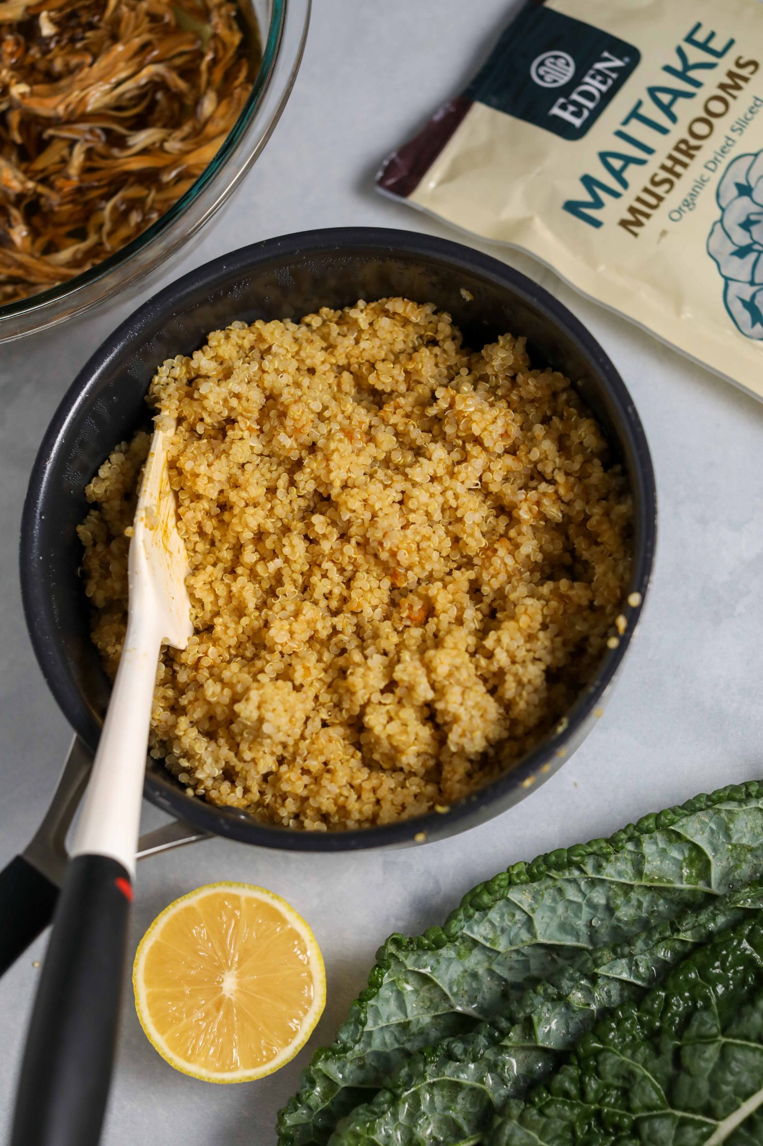 cooked quinoa in pot with spatula with halved lemon and kale and mushrooms soaked in water on the side 