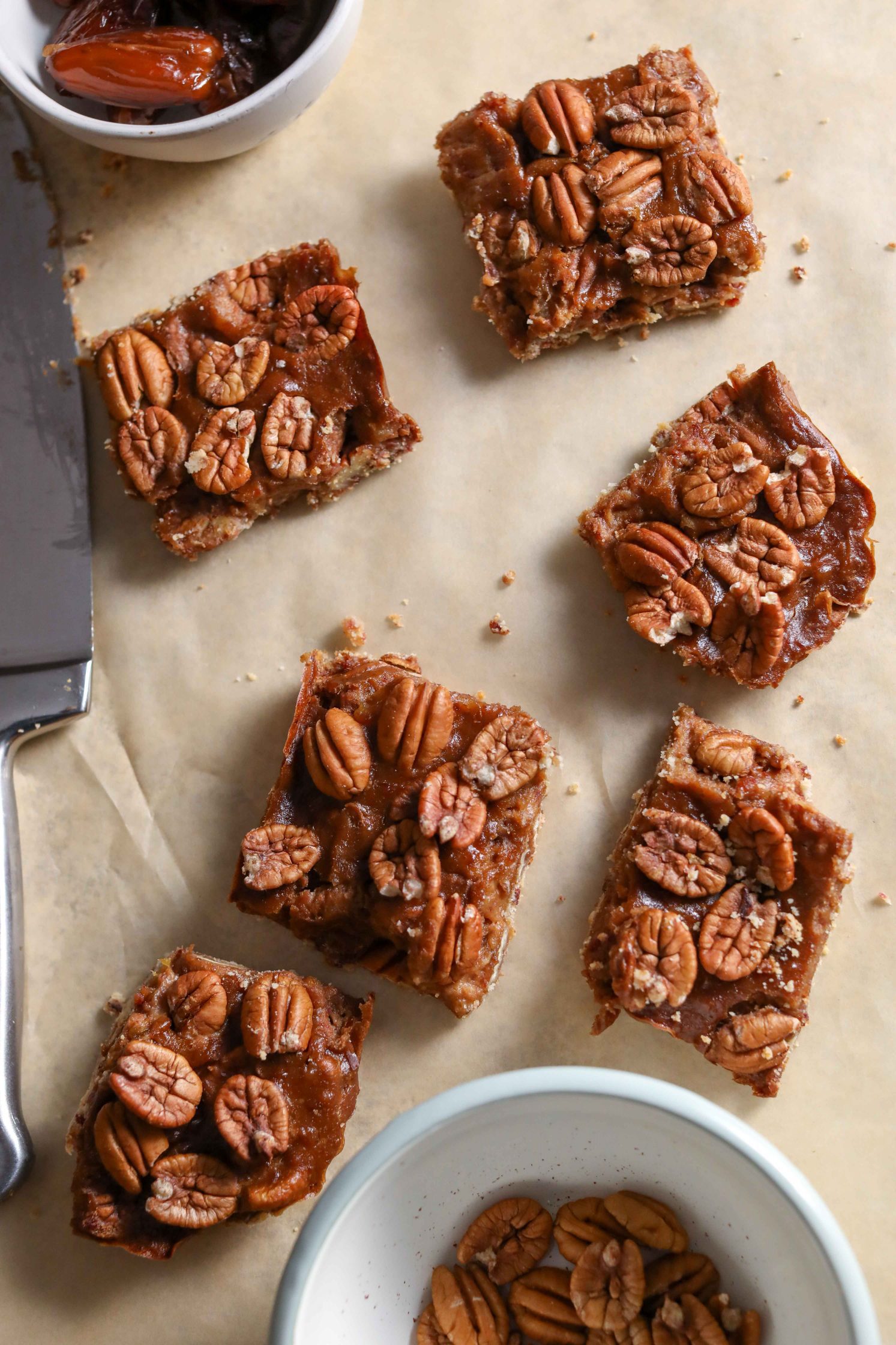Vegan Pecan Pie Bars sliced on parchment paper with knife by Flora & Vino