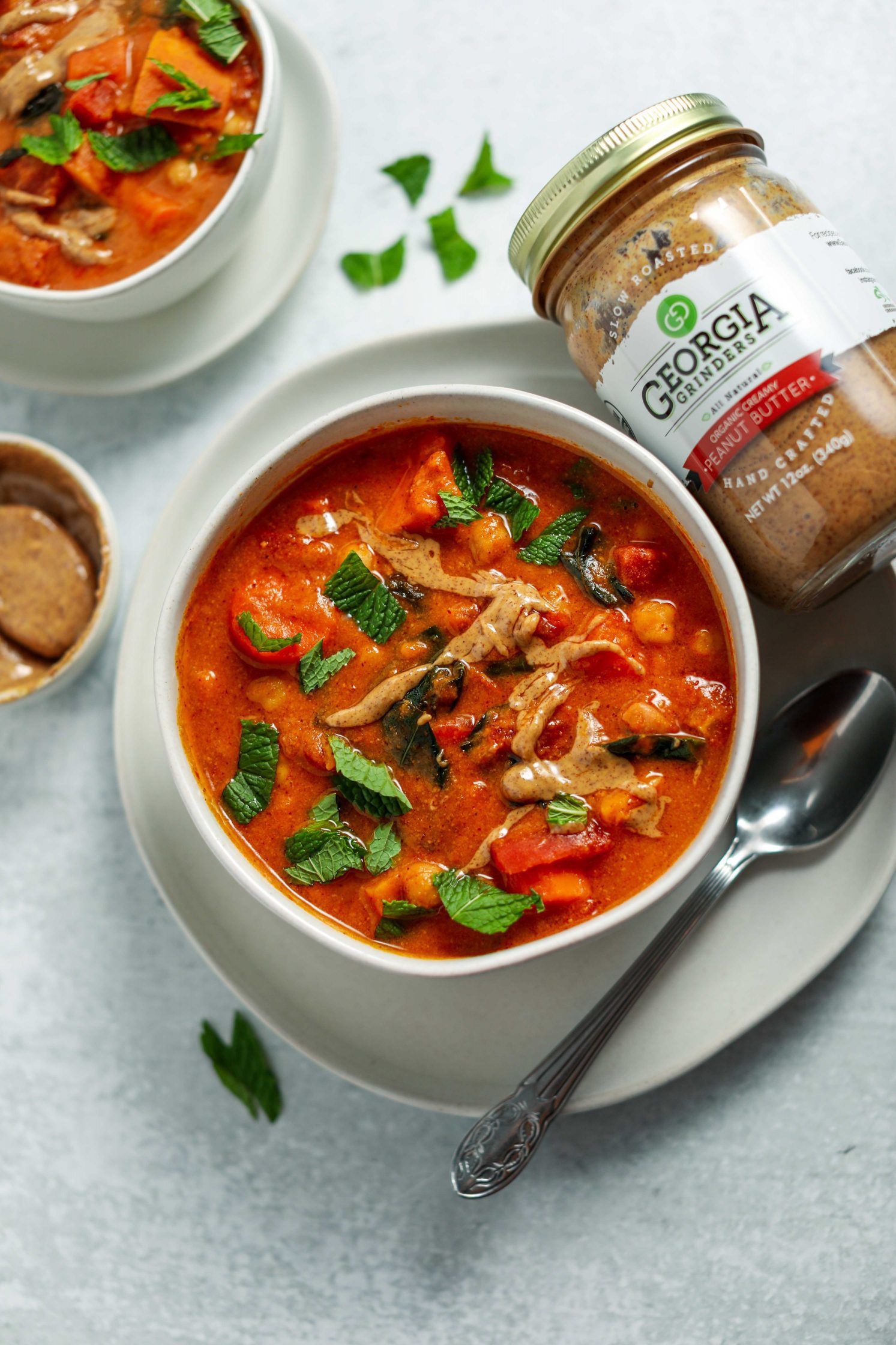 African Peanut Butter Stew served in a bowl on a plate with a spoon and fresh mint on top by Flora & Vino 