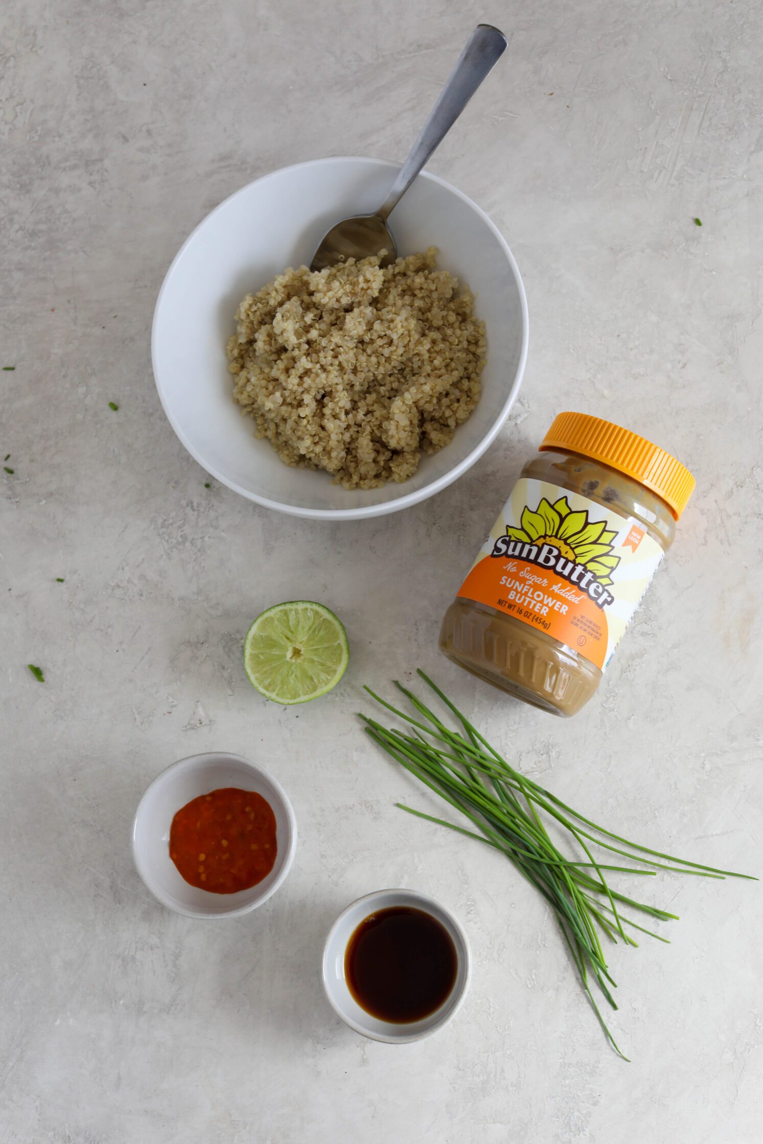 quinoa in a bowl with a jar of SunButter, lime, chives, sriracha, and coconut aminos on wooden board by Flora & Vino