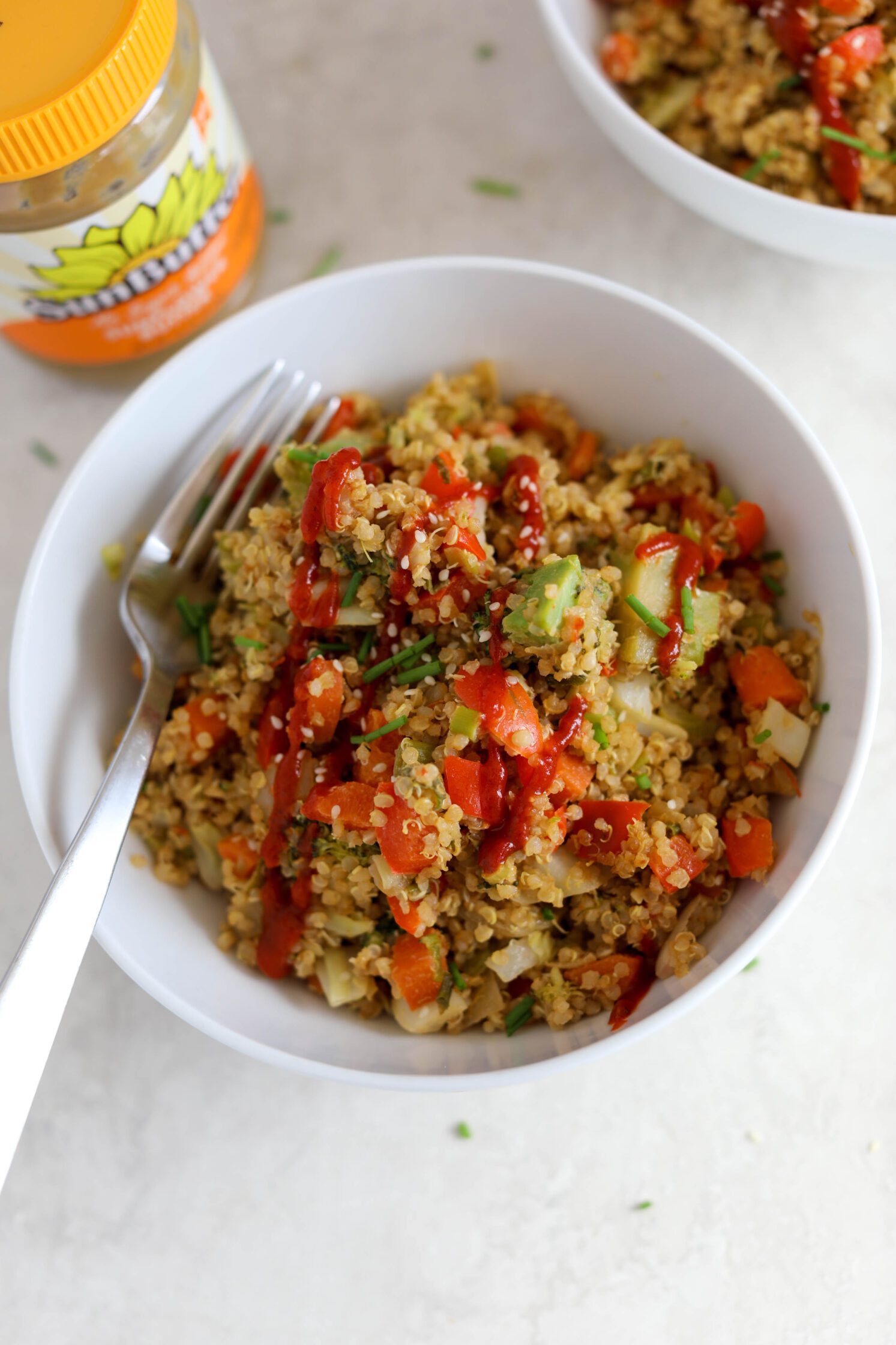 SunButter Quinoa Fried Rice served in a bowl with sriracha, chives, and sesame seeds by Flora & Vino 