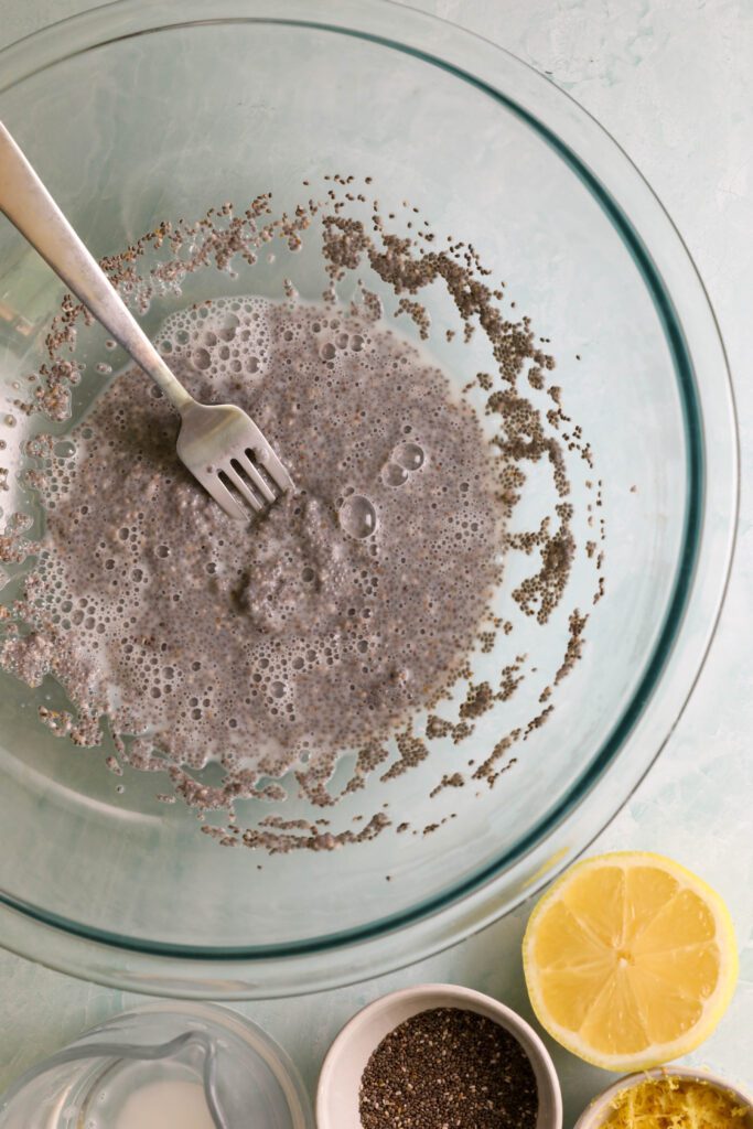 chia seeds and almond milk mixed in large glass bowl with a fork by Flora & Vino with lemon, chia seeds, and lemon zest on the side by Flora & Vino